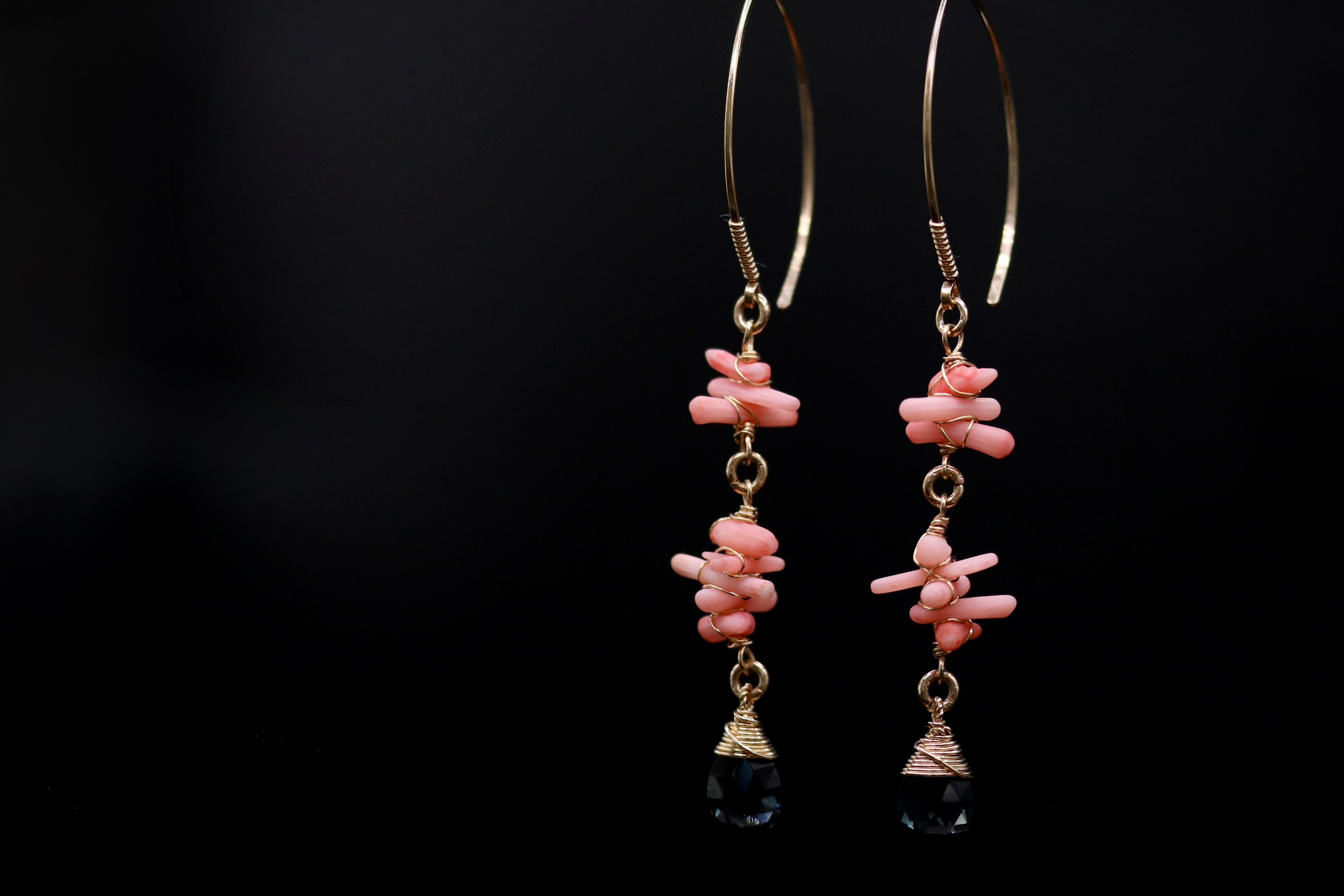 A pair of gold earrings with pink and black beads hanging from them against a black background.