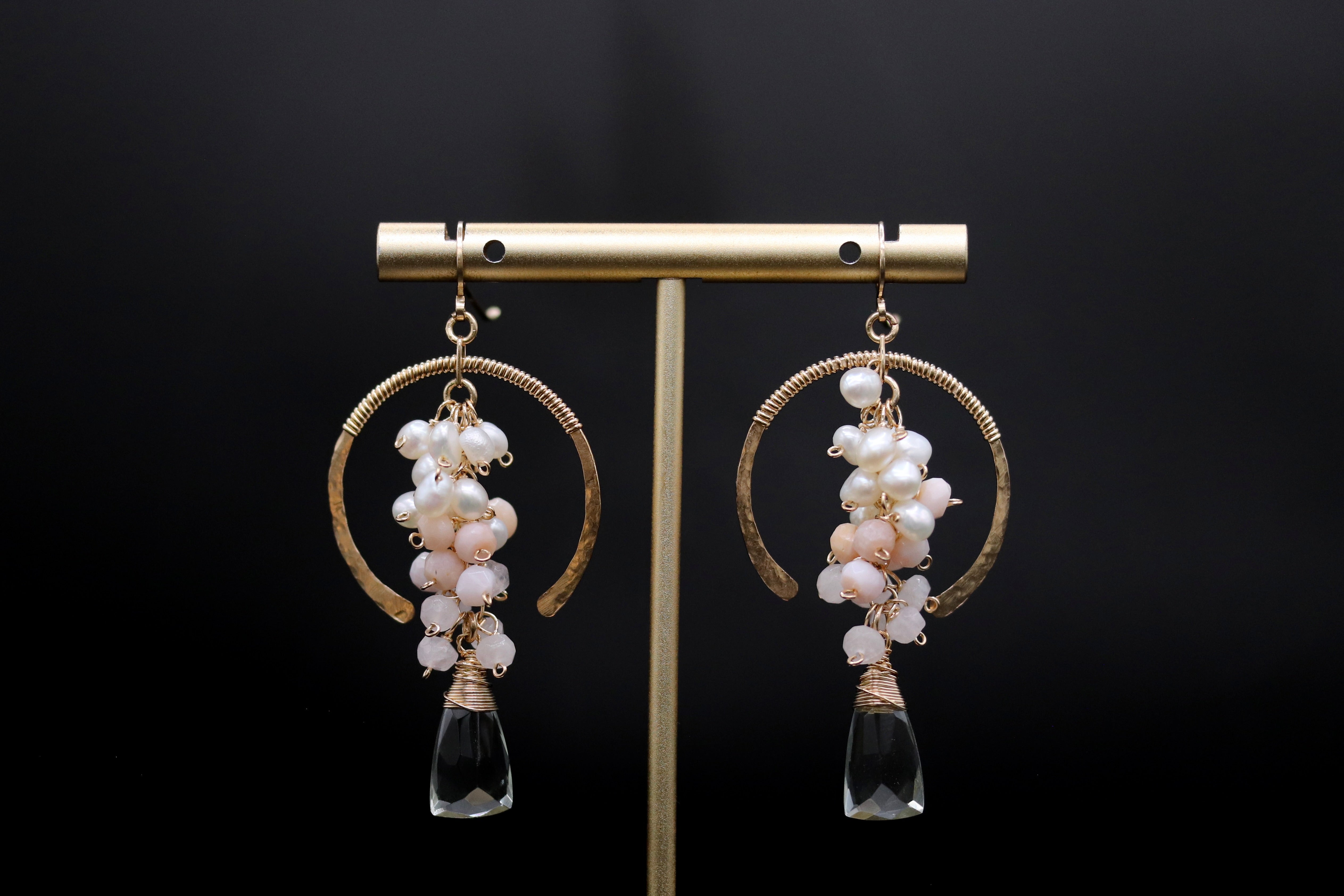 A pair of elegant earrings with a gold-colored metal frame and dangling clear glass pendants, adorned with white and pink pearls.