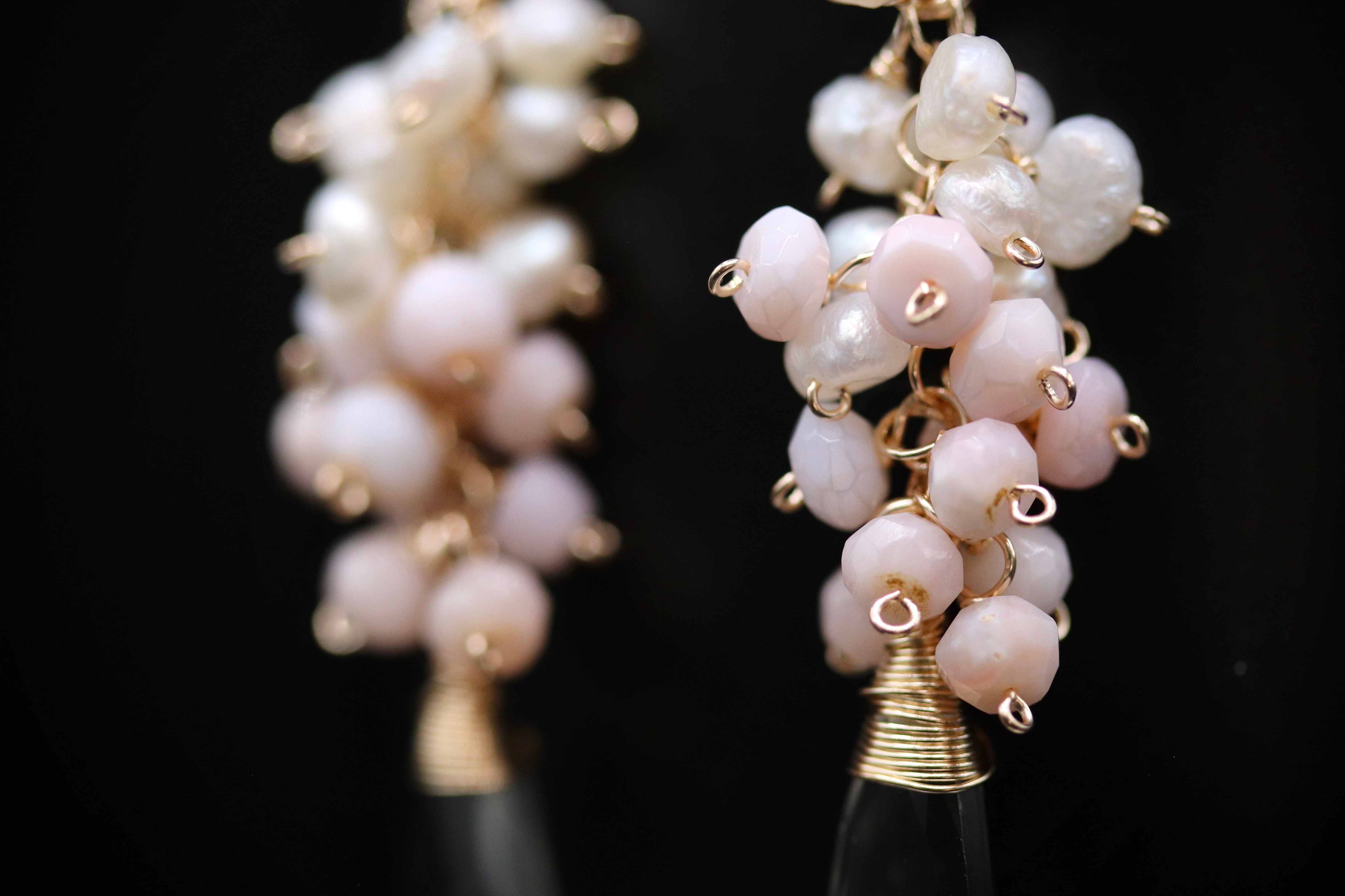 A close-up view of a pair of earrings with white and pink beads, each adorned with a gold-colored metal hook.