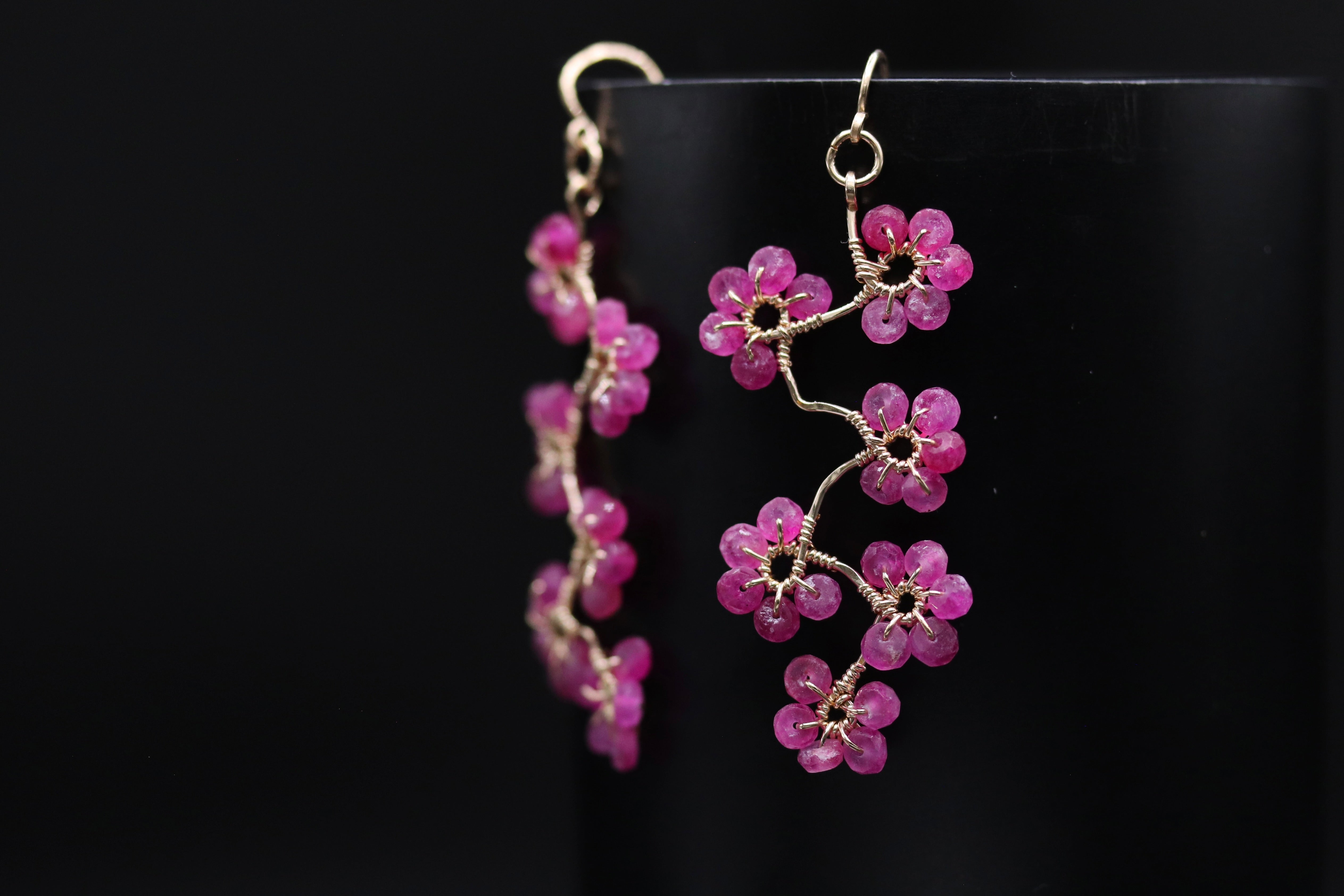 A pair of delicate earrings with a floral design, featuring small pink gemstones arranged in a cascading pattern.