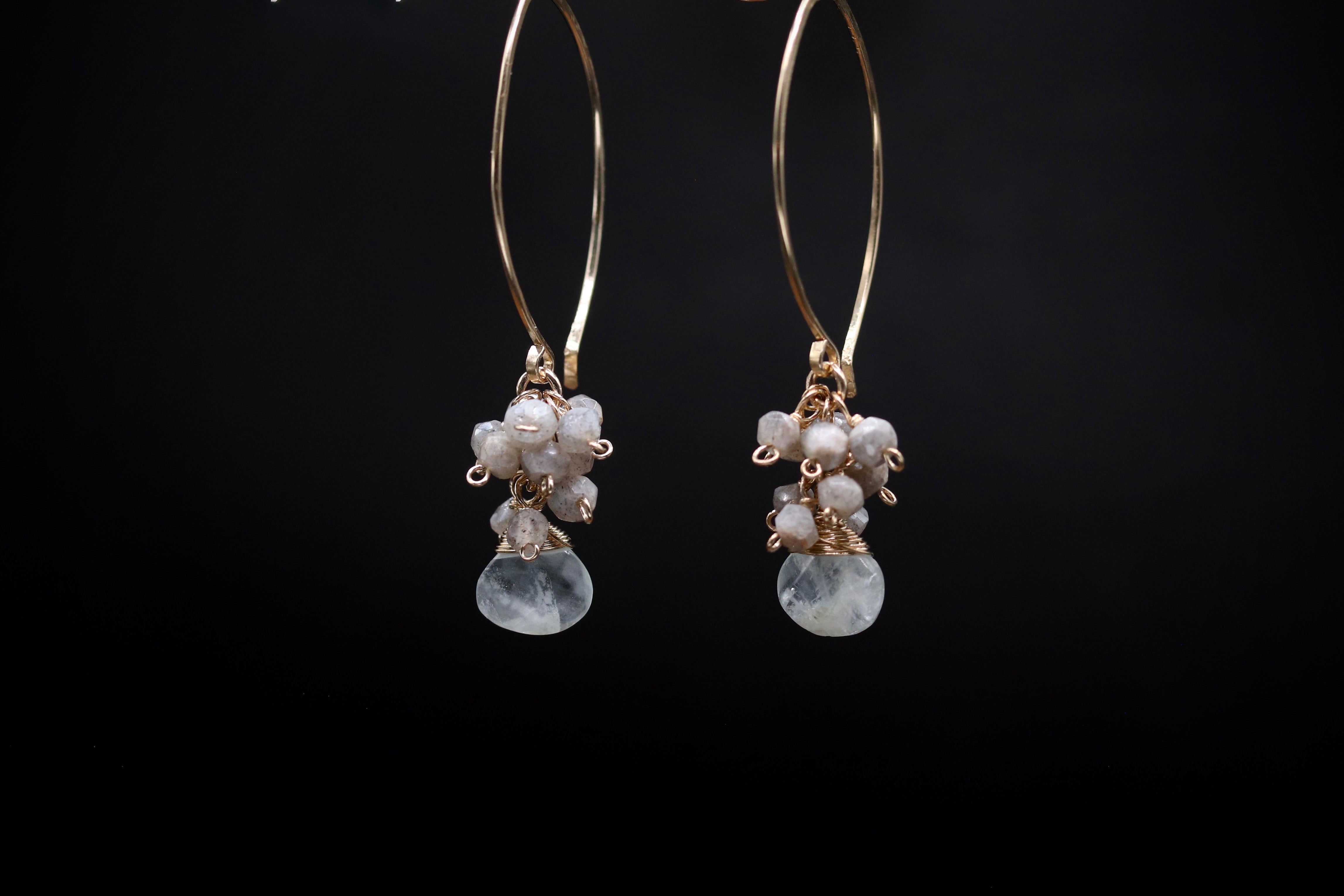 A pair of gold hoop earrings with white stones hanging from them against a black background.