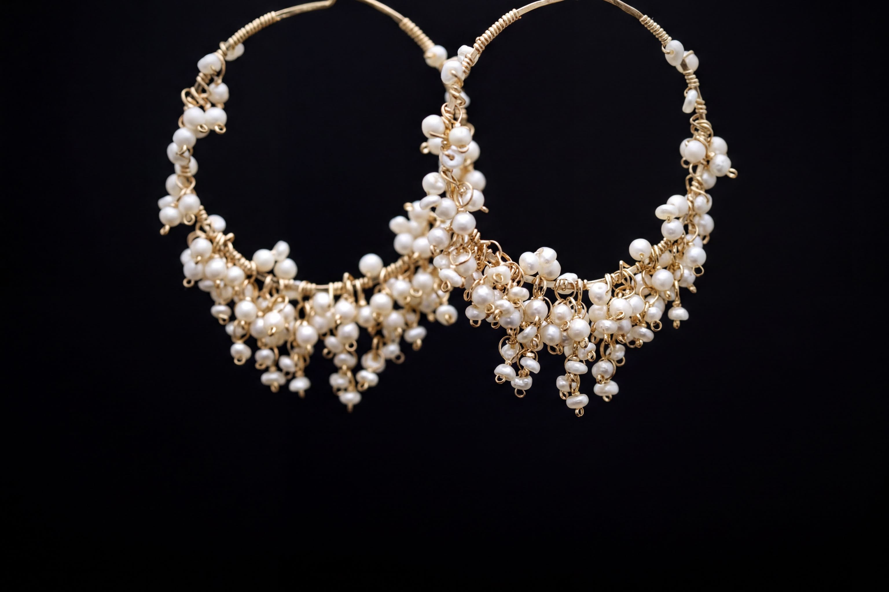 A pair of elegant earrings made of white pearls and gold wire, displayed against a black background.