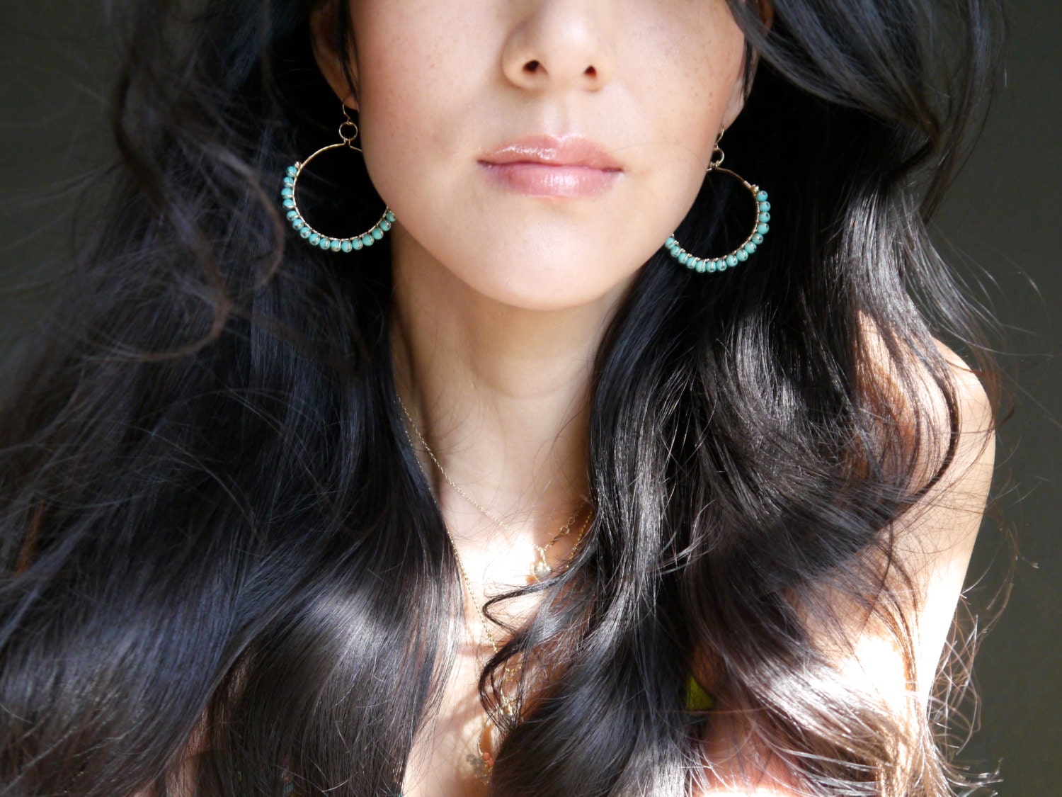 May include: A pair of gold hoop earrings with turquoise beads. The earrings are worn by a person with long black hair.