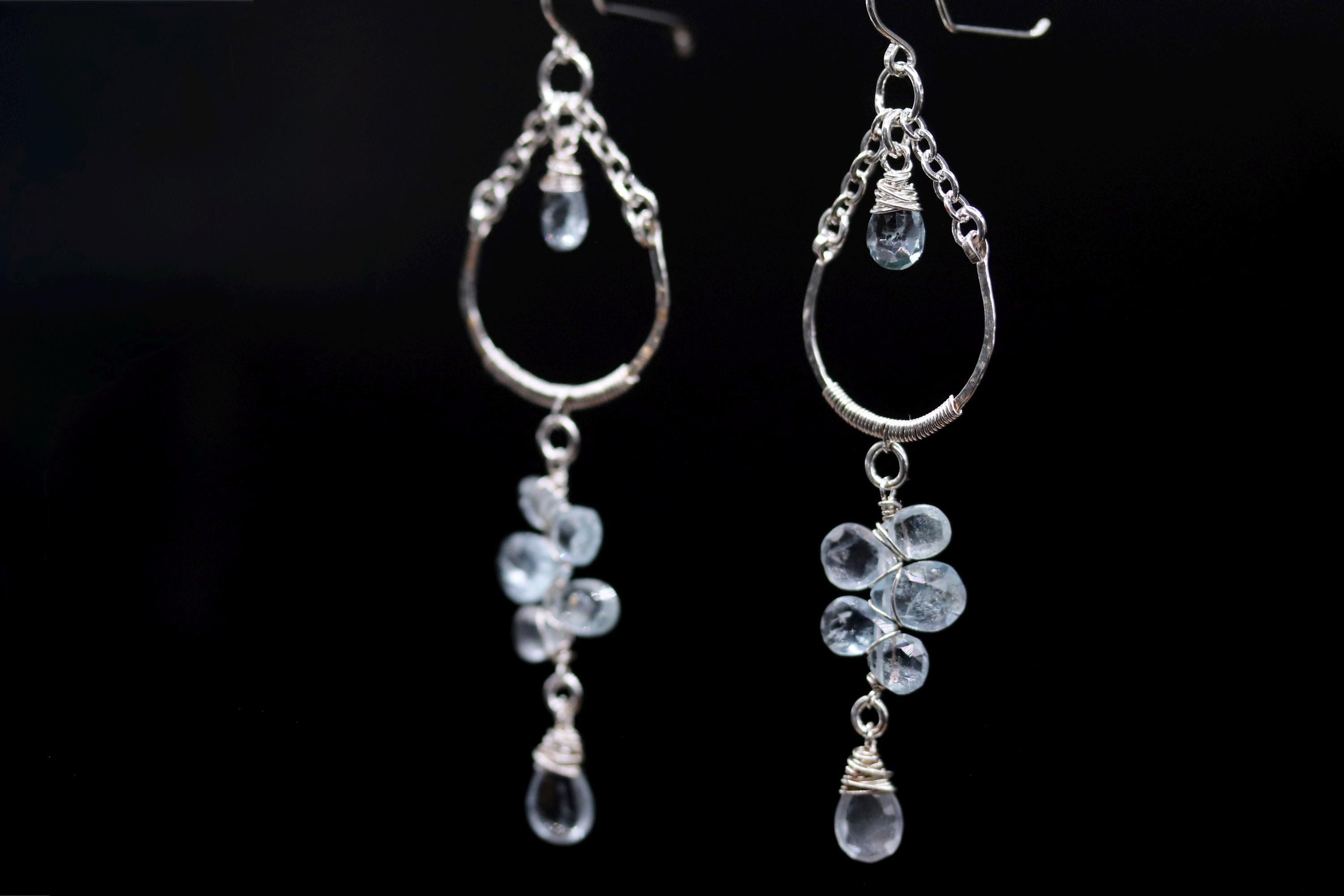 A pair of elegant earrings with clear gemstone accents hanging from the bottom of the earrings against a black background.