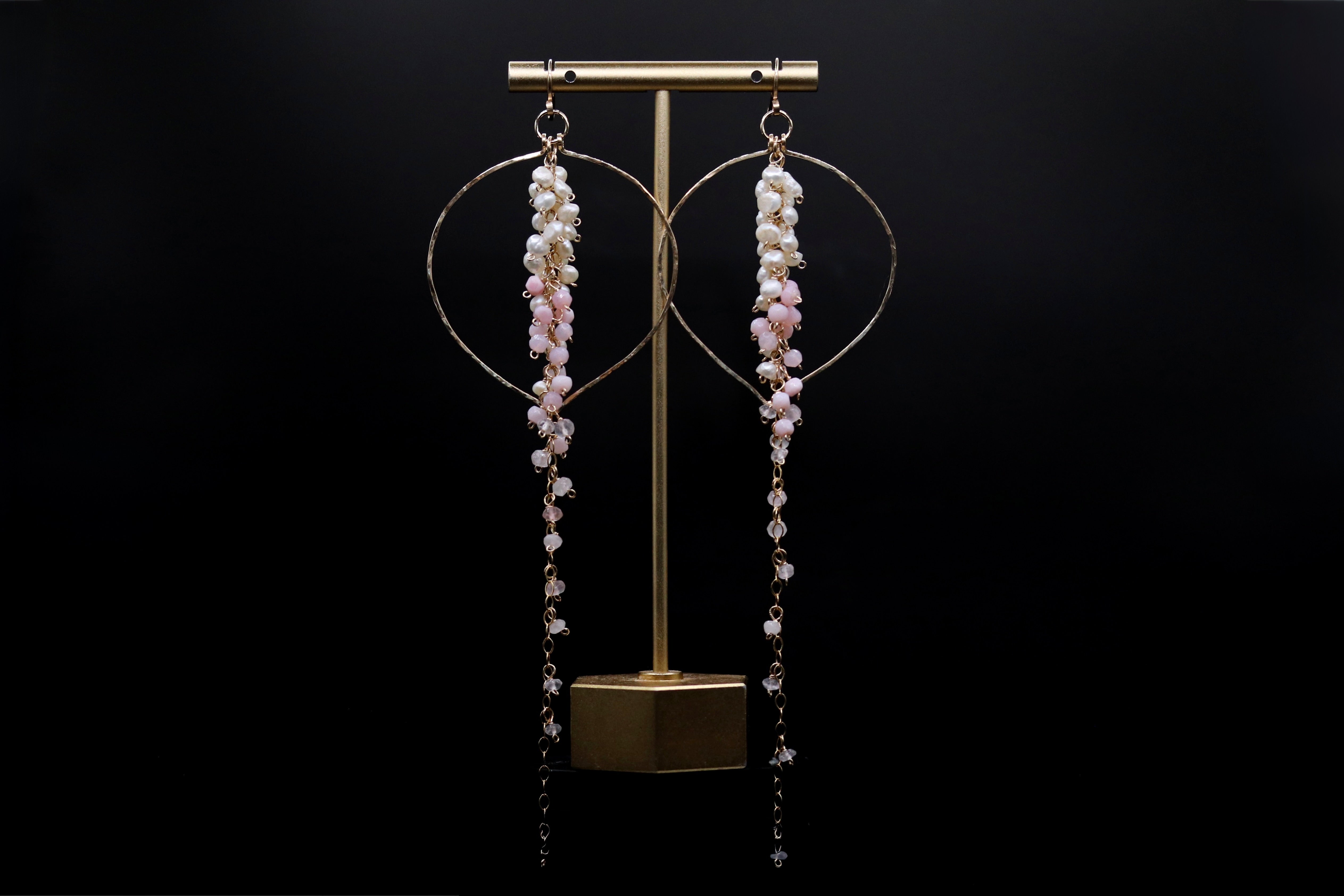 A pair of elegant earrings with long, dangling chains and small, round beads hanging from them, displayed on a gold stand against a black background.