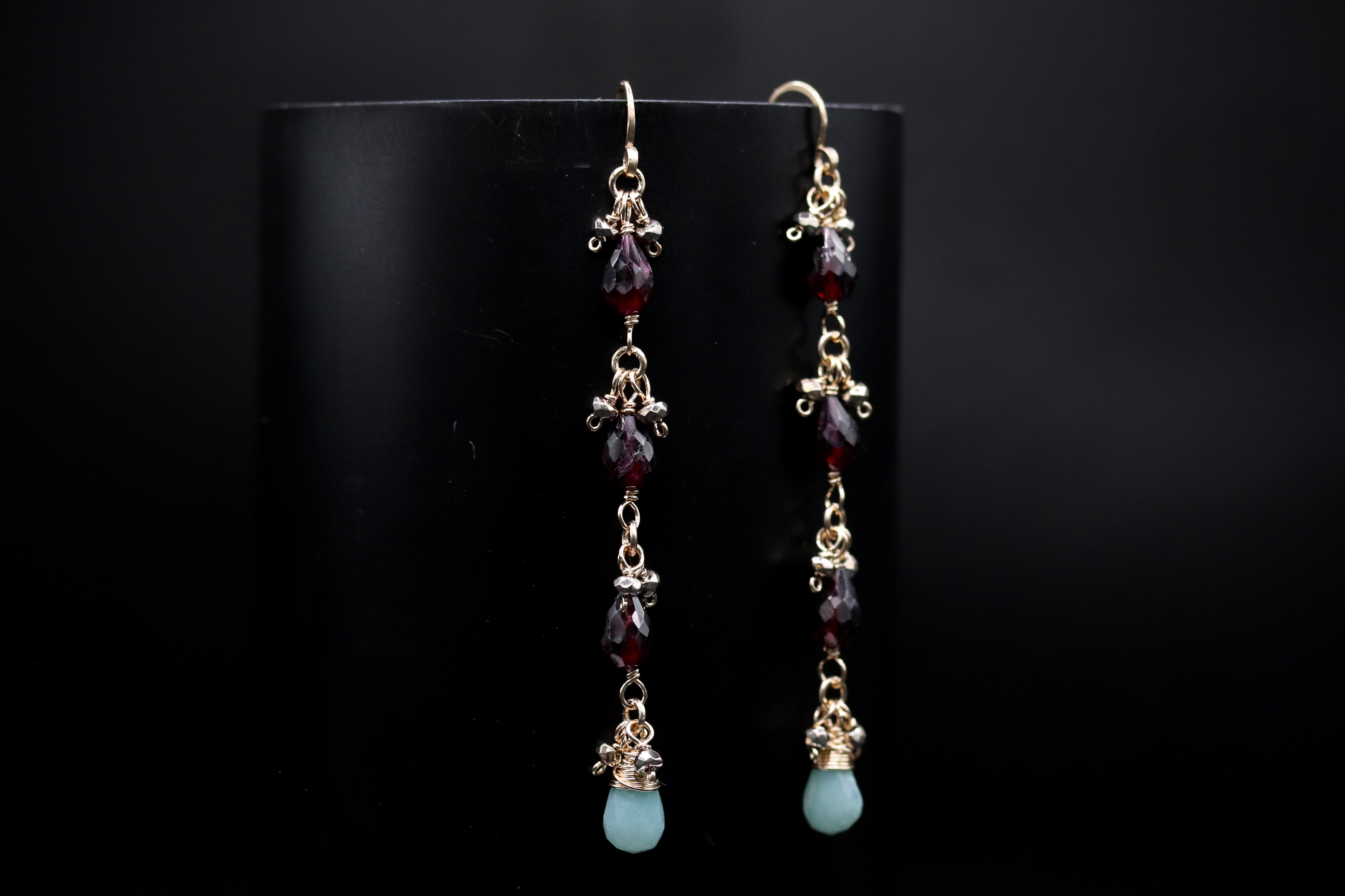 A pair of elegant earrings with a black background and gold accents, featuring a row of dangling gemstones in various colors.