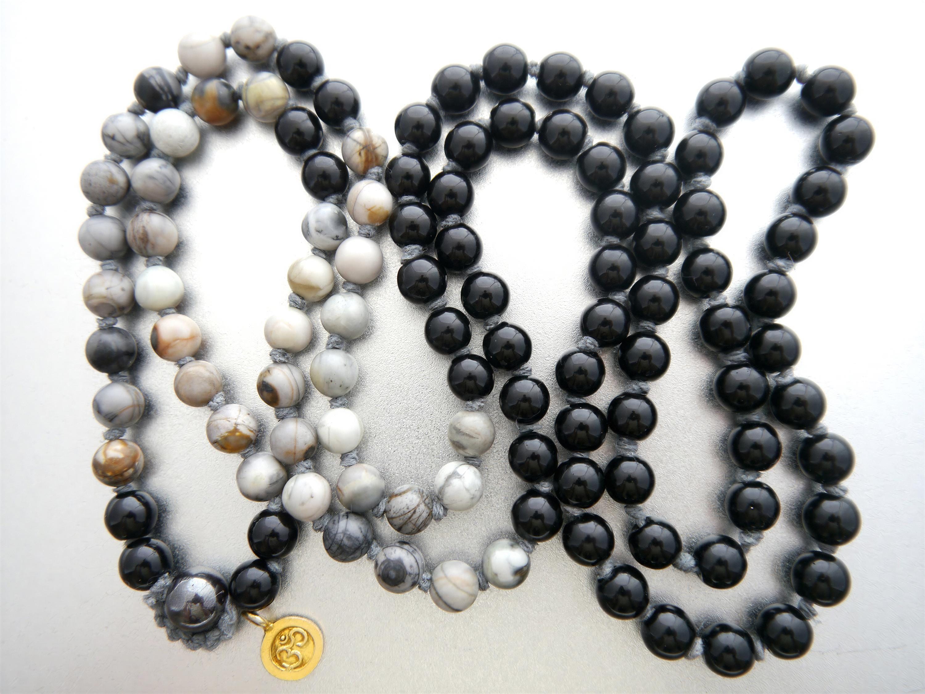 three necklaces with different colored beads, including black, gray, and white beads, arranged in a row.