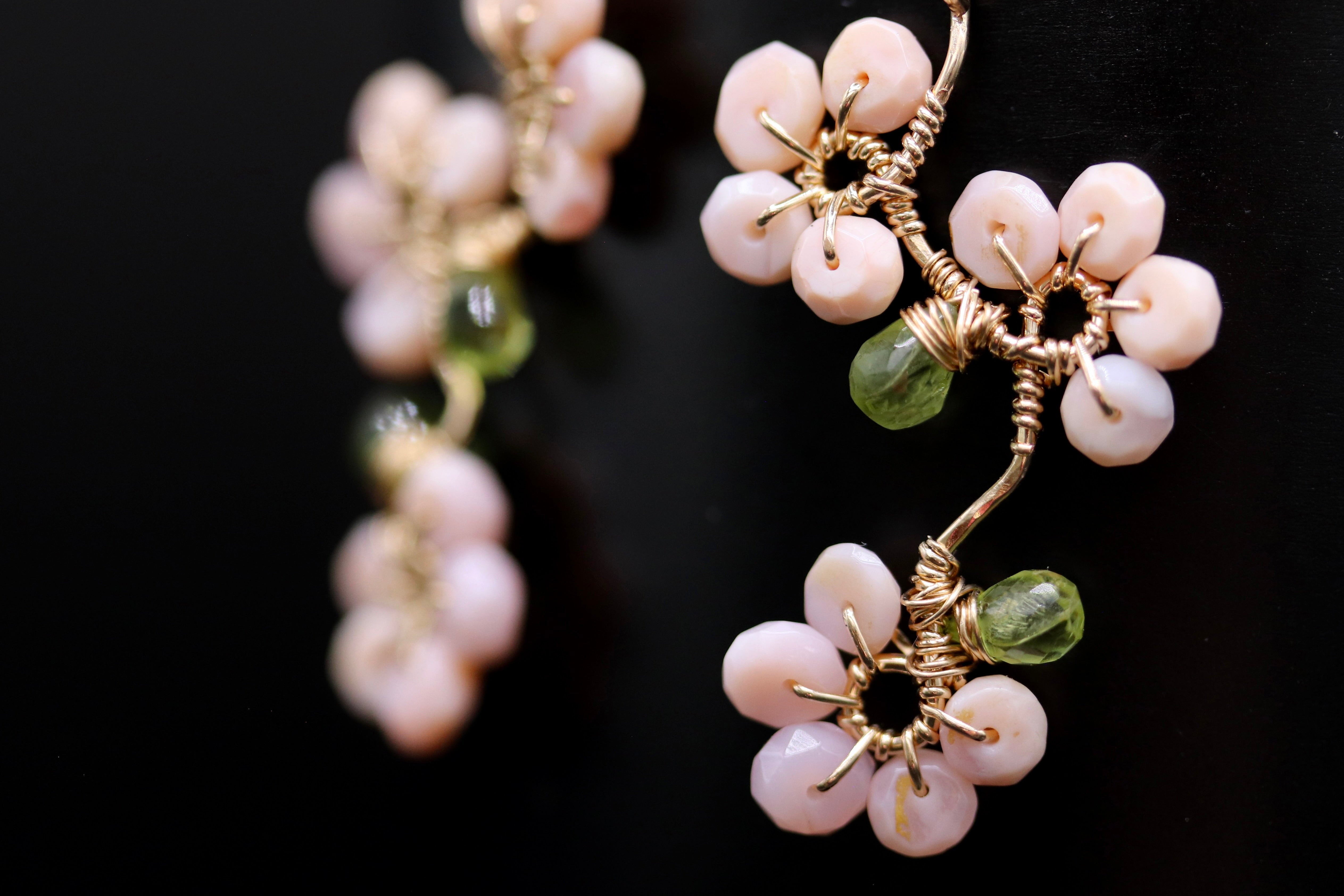 A close-up view of a pair of delicate earrings with a floral design, featuring small white beads and green stones.