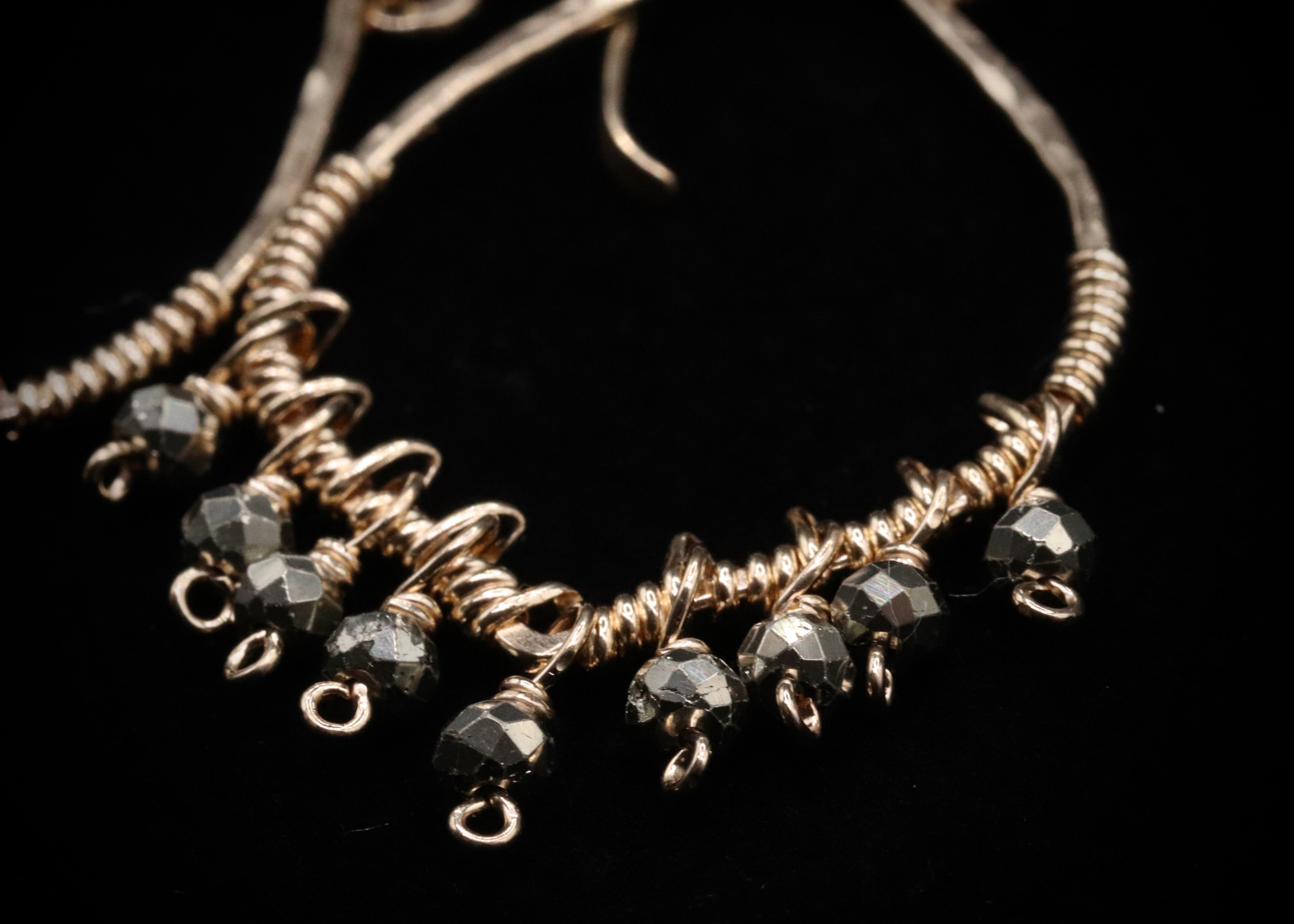 A close-up view of a pair of earrings with a twisted metal design and small black beads hanging from it.