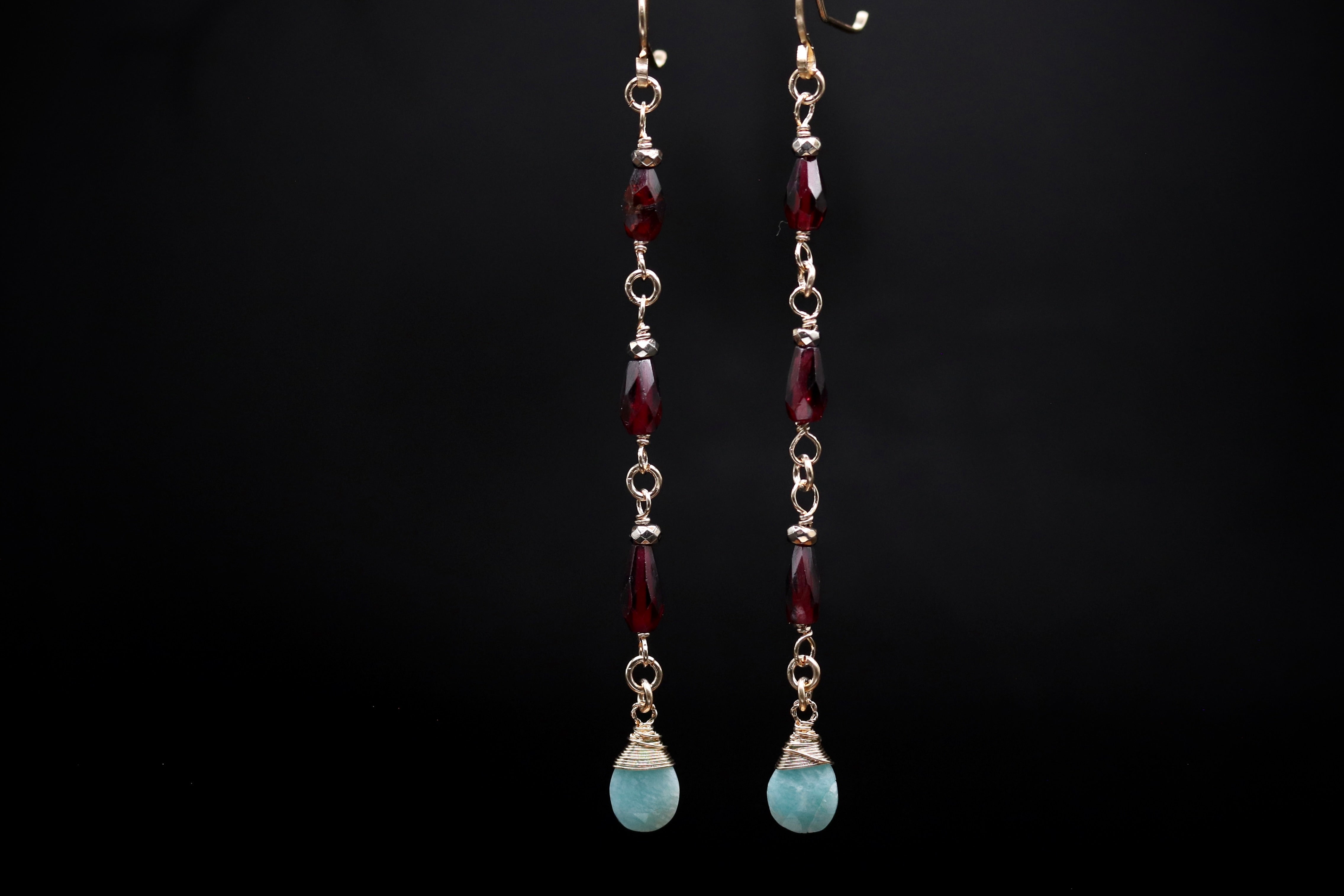 A pair of earrings with a combination of red and blue gemstones, suspended from gold chains against a black background.