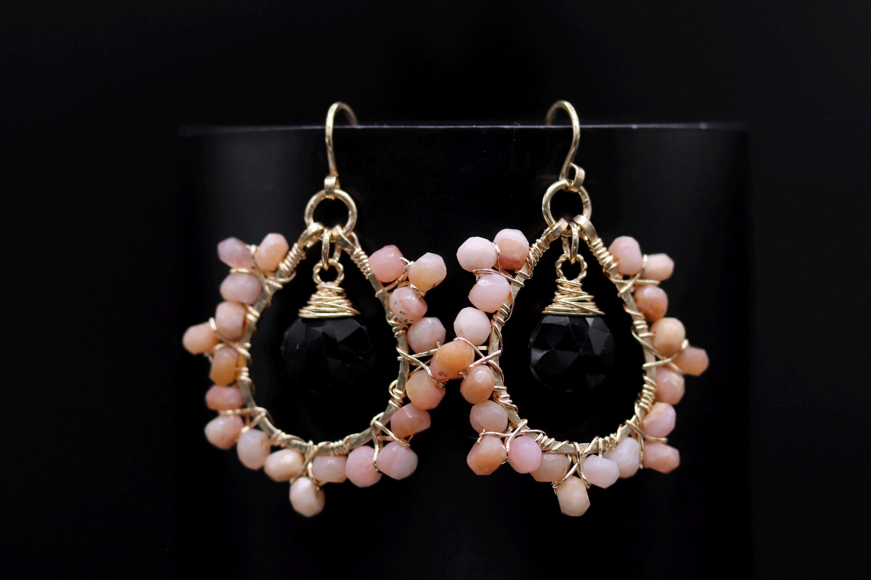 A pair of elegant earrings with black stones and pink beads, displayed against a black background.
