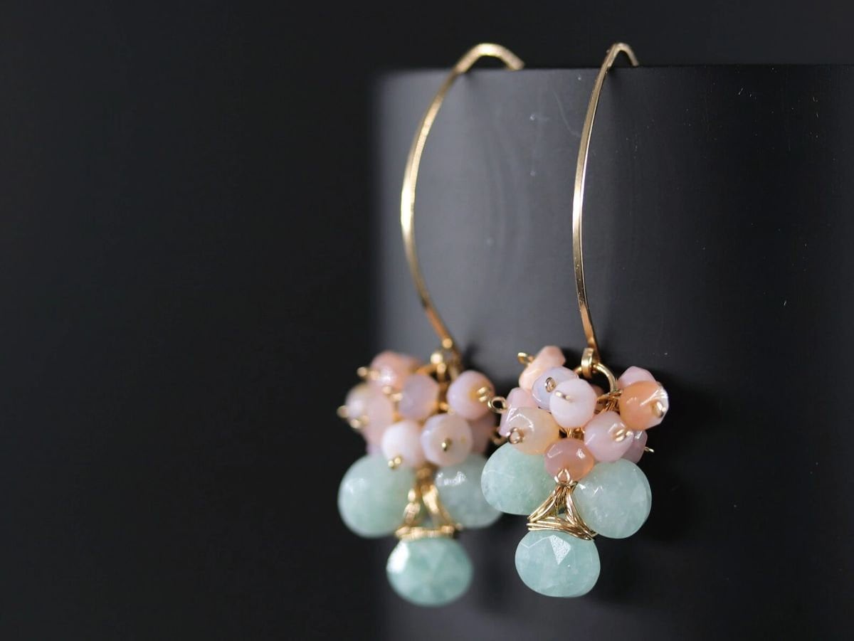May include: Gold-tone earrings with clusters of small, round, and faceted beads in shades of pink, peach, and light green. The earrings have a curved, wire design.
