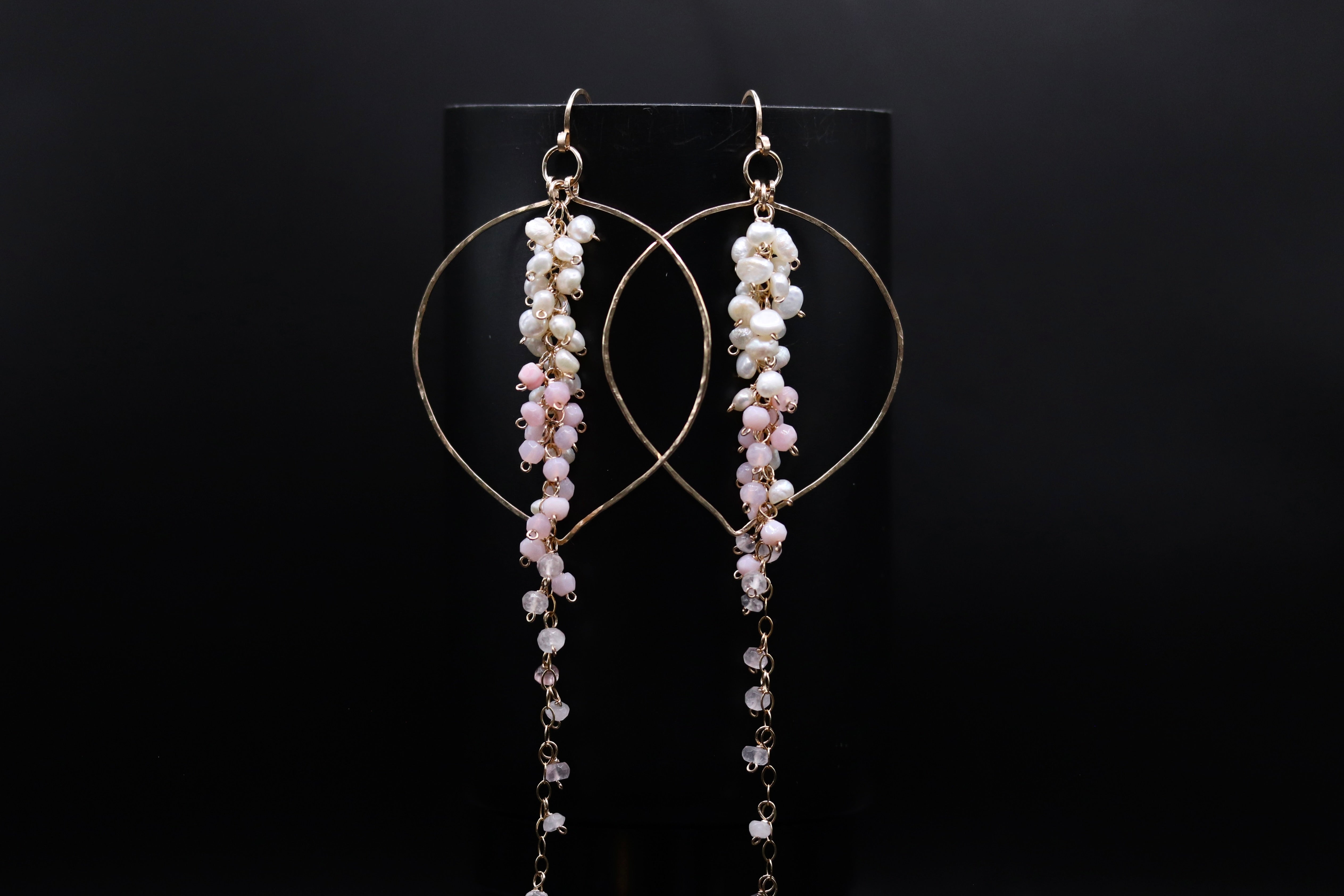 A pair of elegant earrings with a black background. The earrings have a circular design with a hoop and are adorned with small white beads hanging from the bottom.