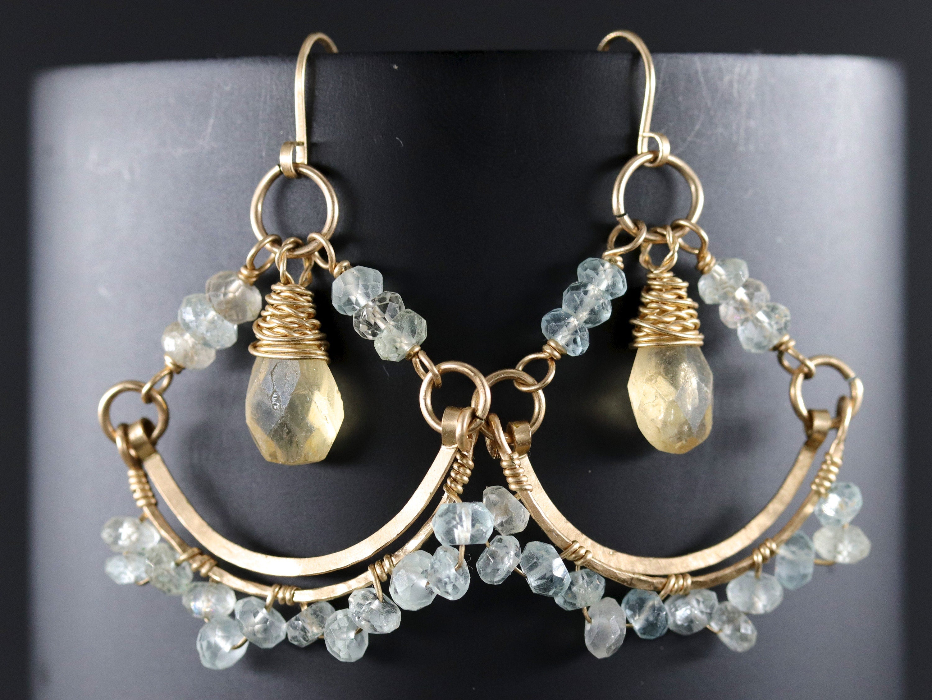 May include: Gold earrings with a teardrop-shaped yellow gemstone and aquamarine beads hanging from a curved wire frame.