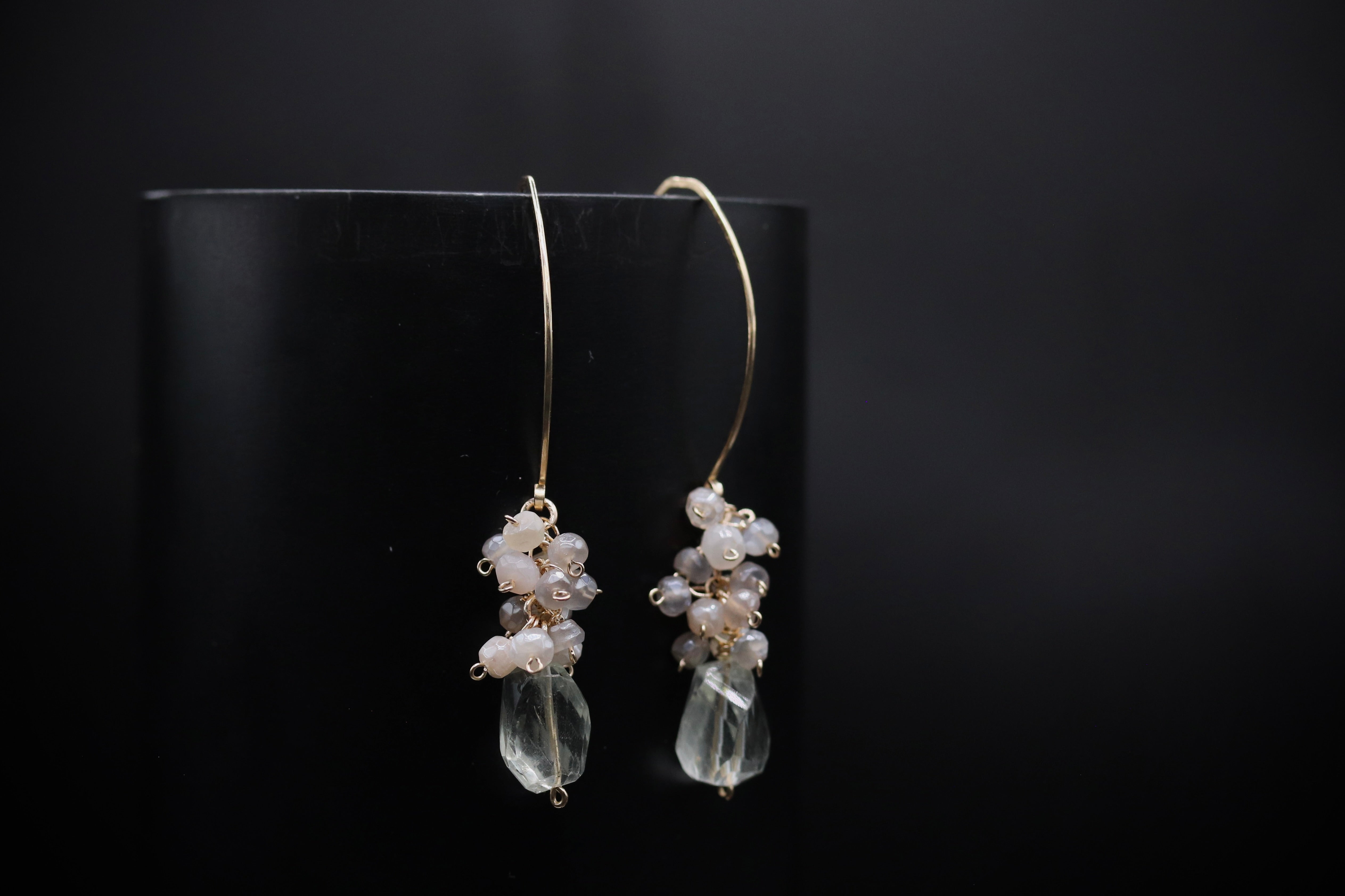 A pair of elegant earrings with clear gemstone pendants and white pearl accents, displayed against a dark background.