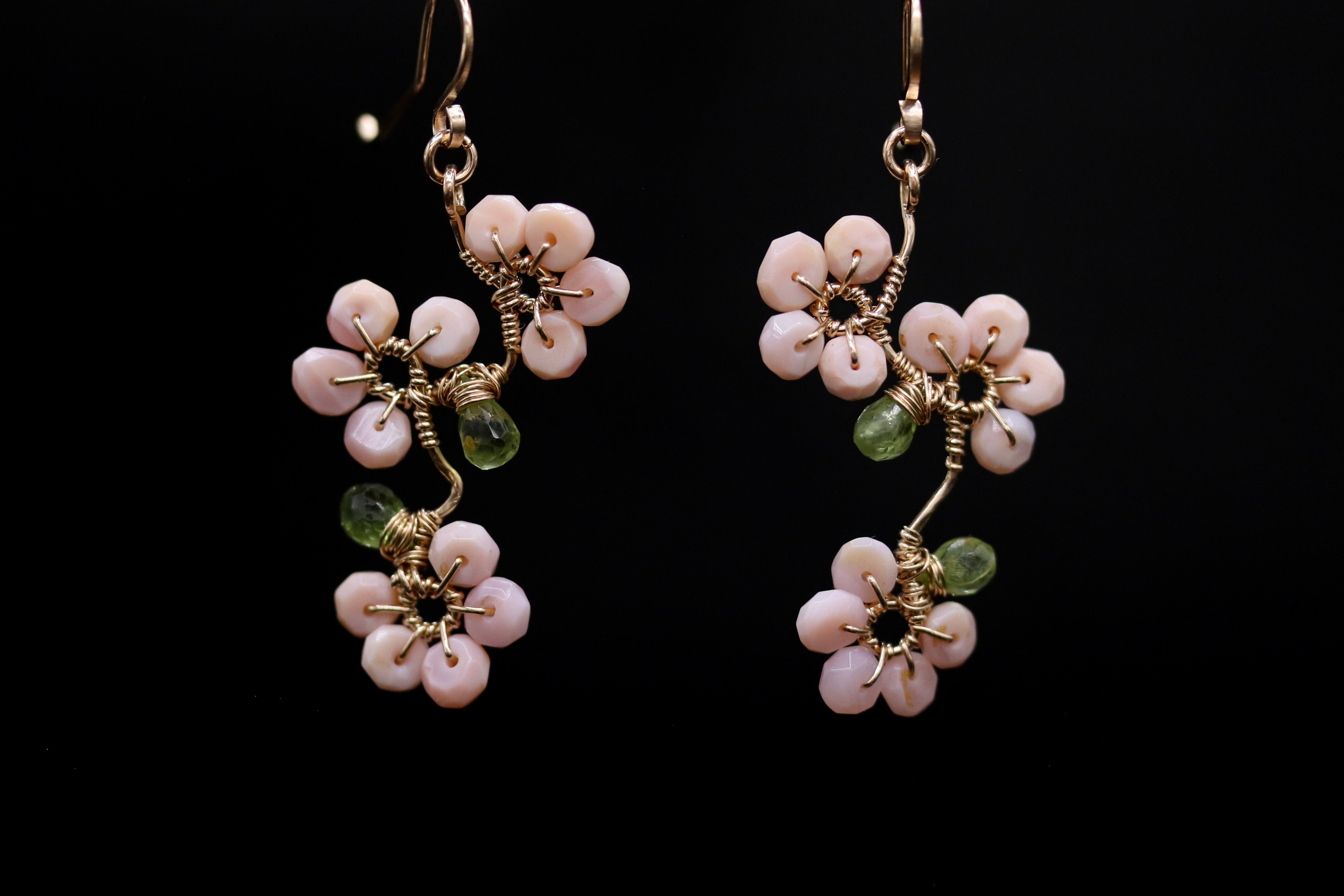 A pair of delicate earrings with pink flowers and green stones, set against a black background.