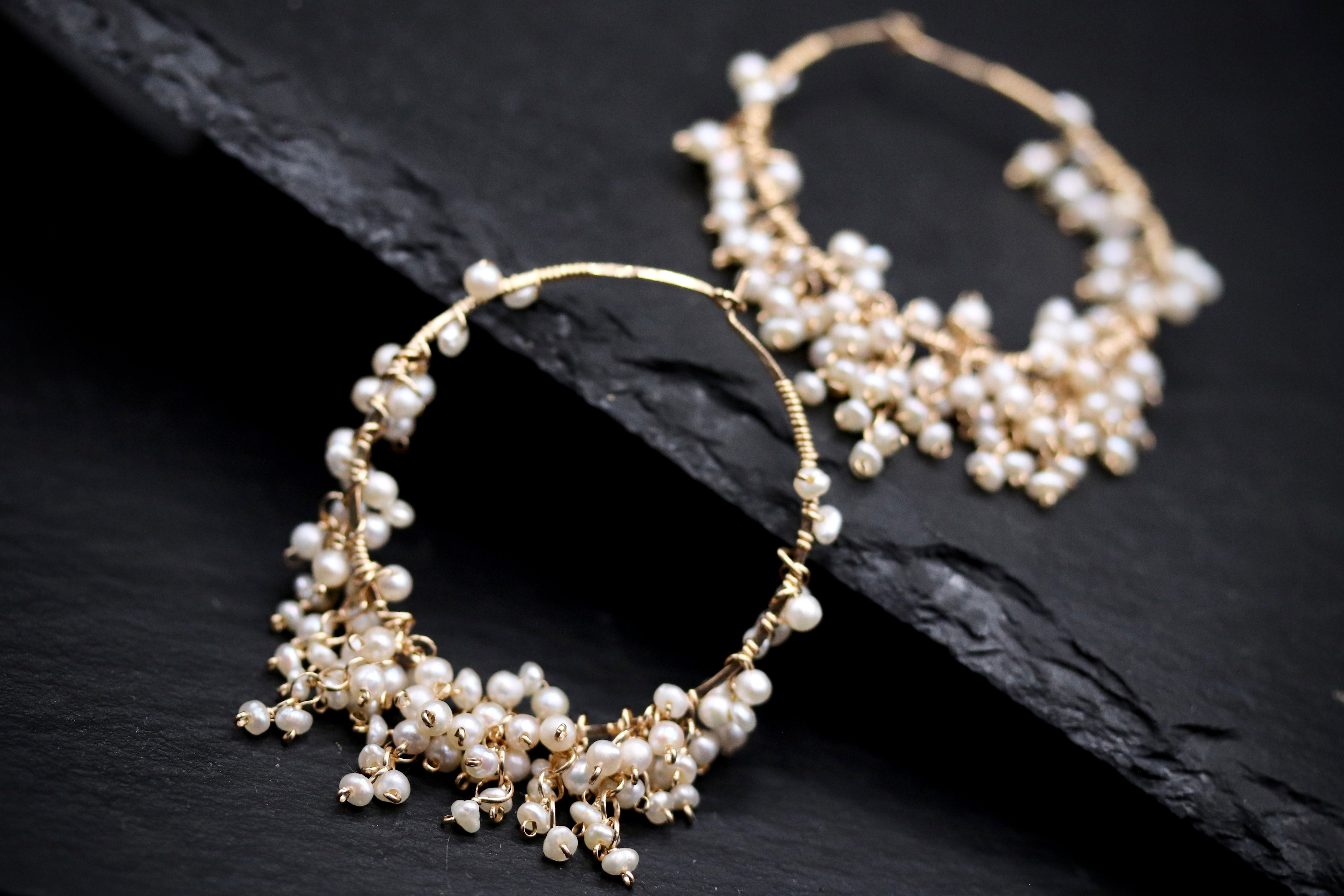 A pair of elegant gold hoop earrings adorned with numerous small white pearls, creating a delicate and sophisticated appearance.