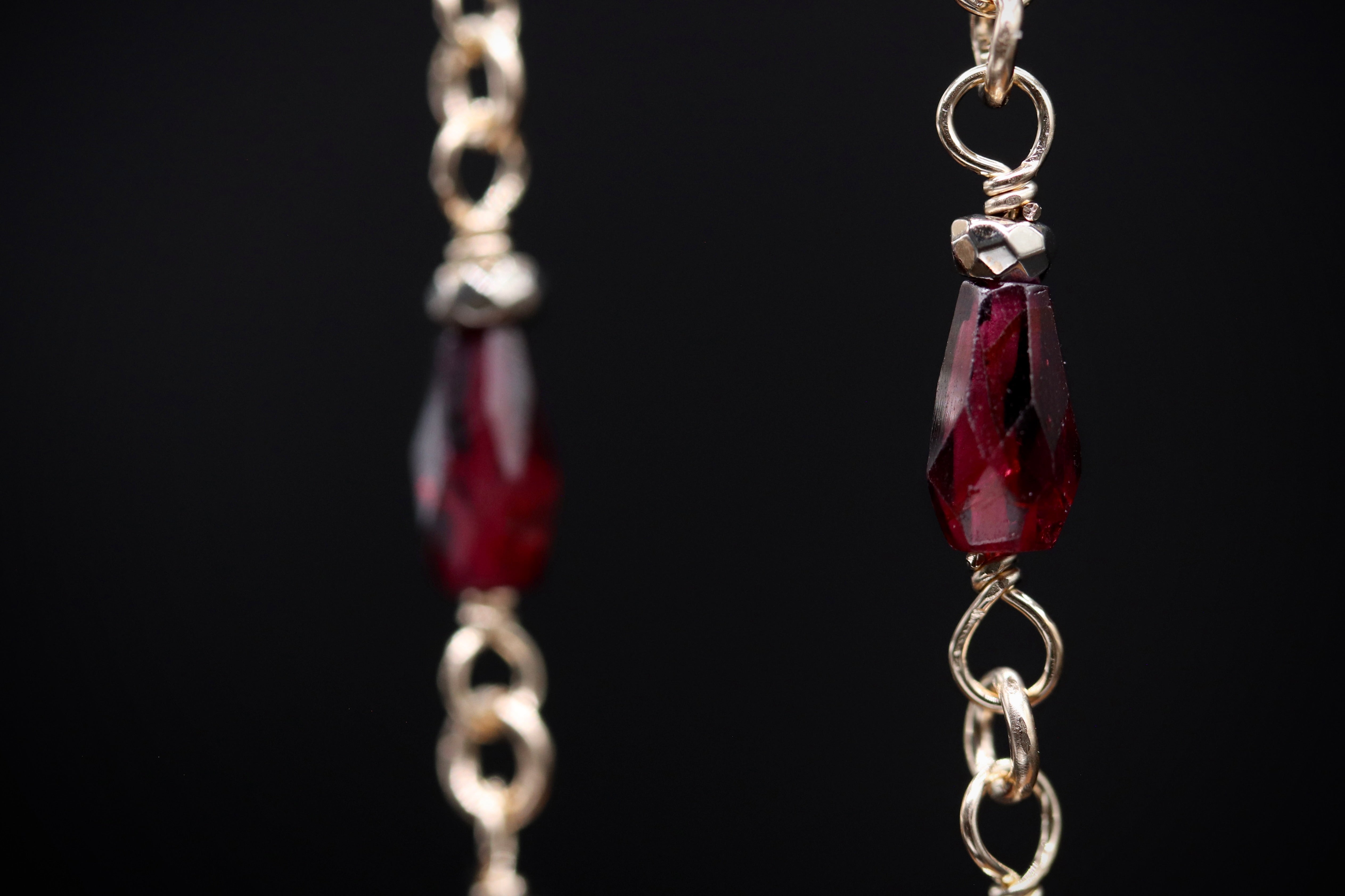 A close-up view of a pair of gold-colored earrings with red gemstones, set in a chain-link design.