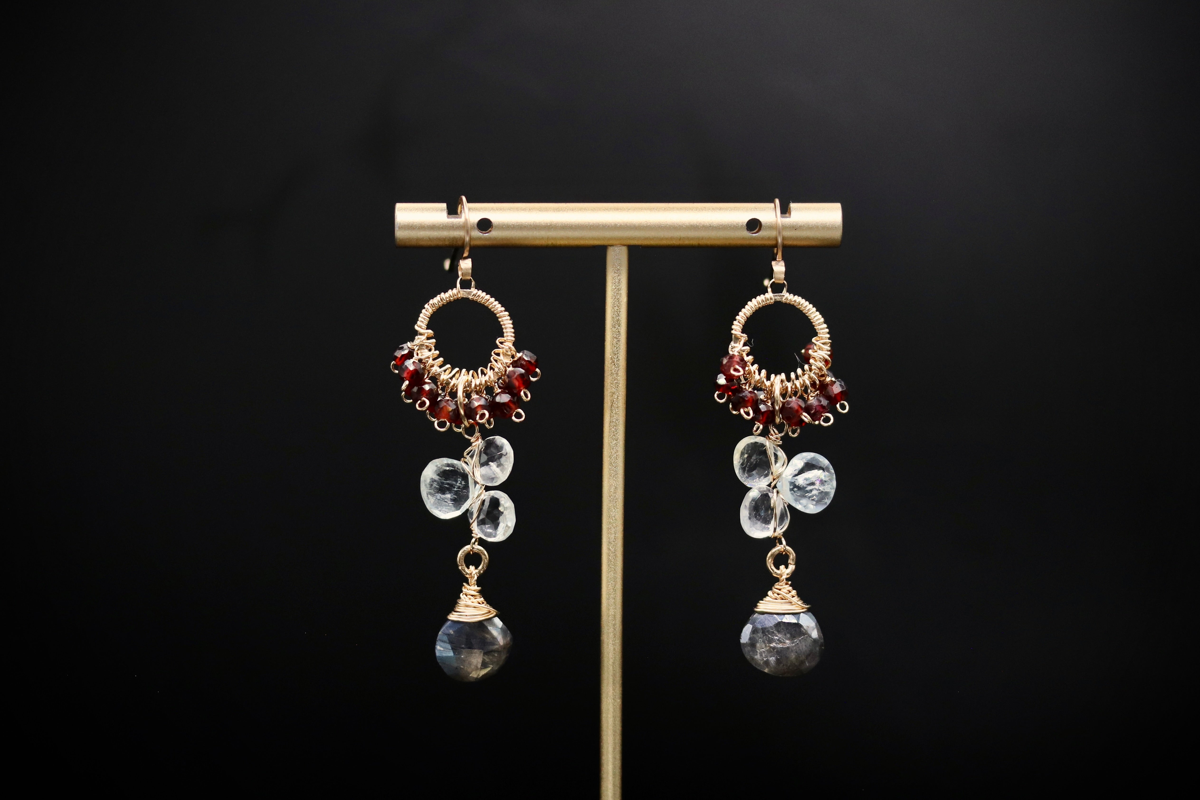 A pair of elegant earrings with clear gemstones and gold-toned metal accents, displayed on a gold stand against a black background.