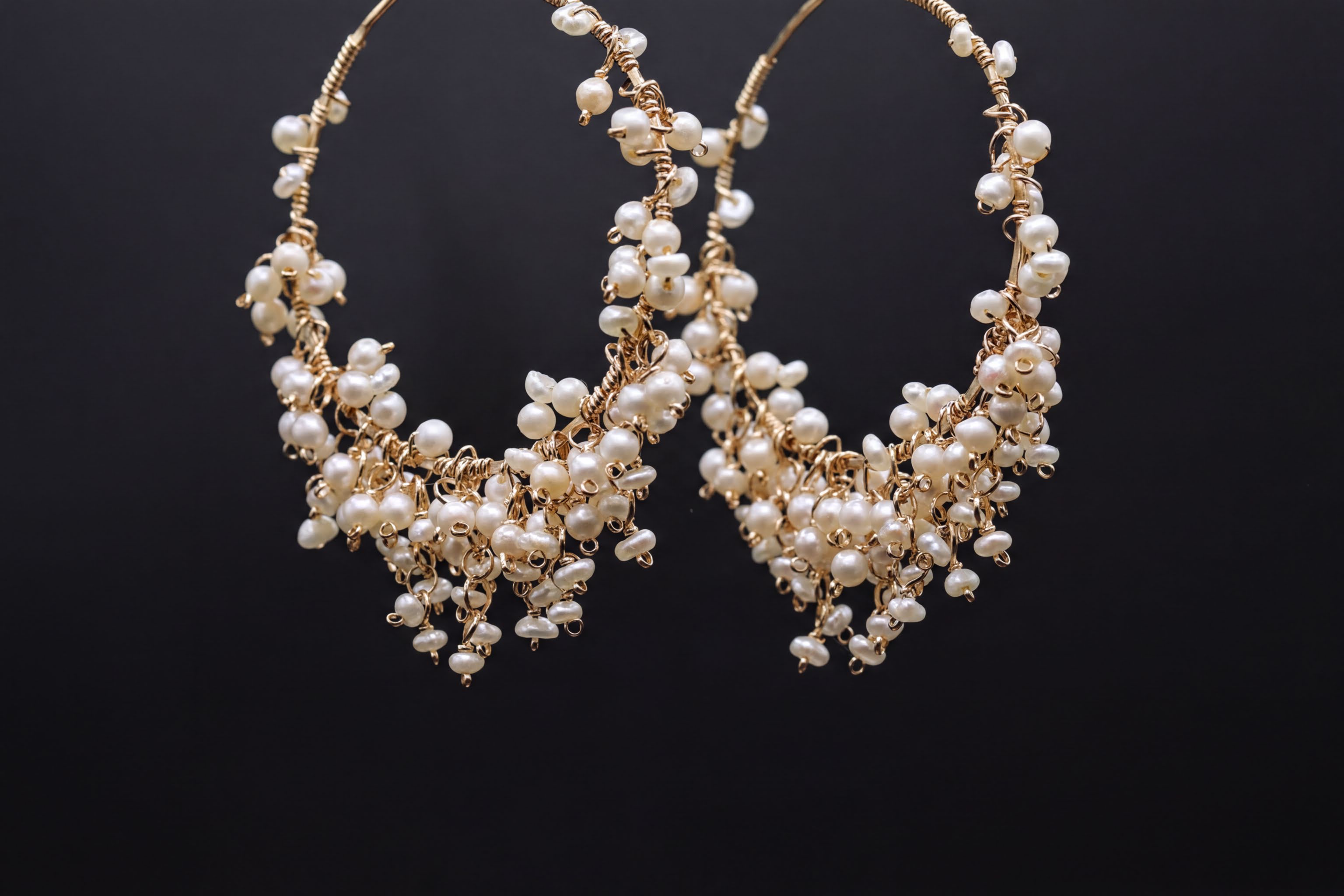 A pair of elegant gold hoop earrings adorned with numerous small white pearls, creating a delicate and sophisticated design.