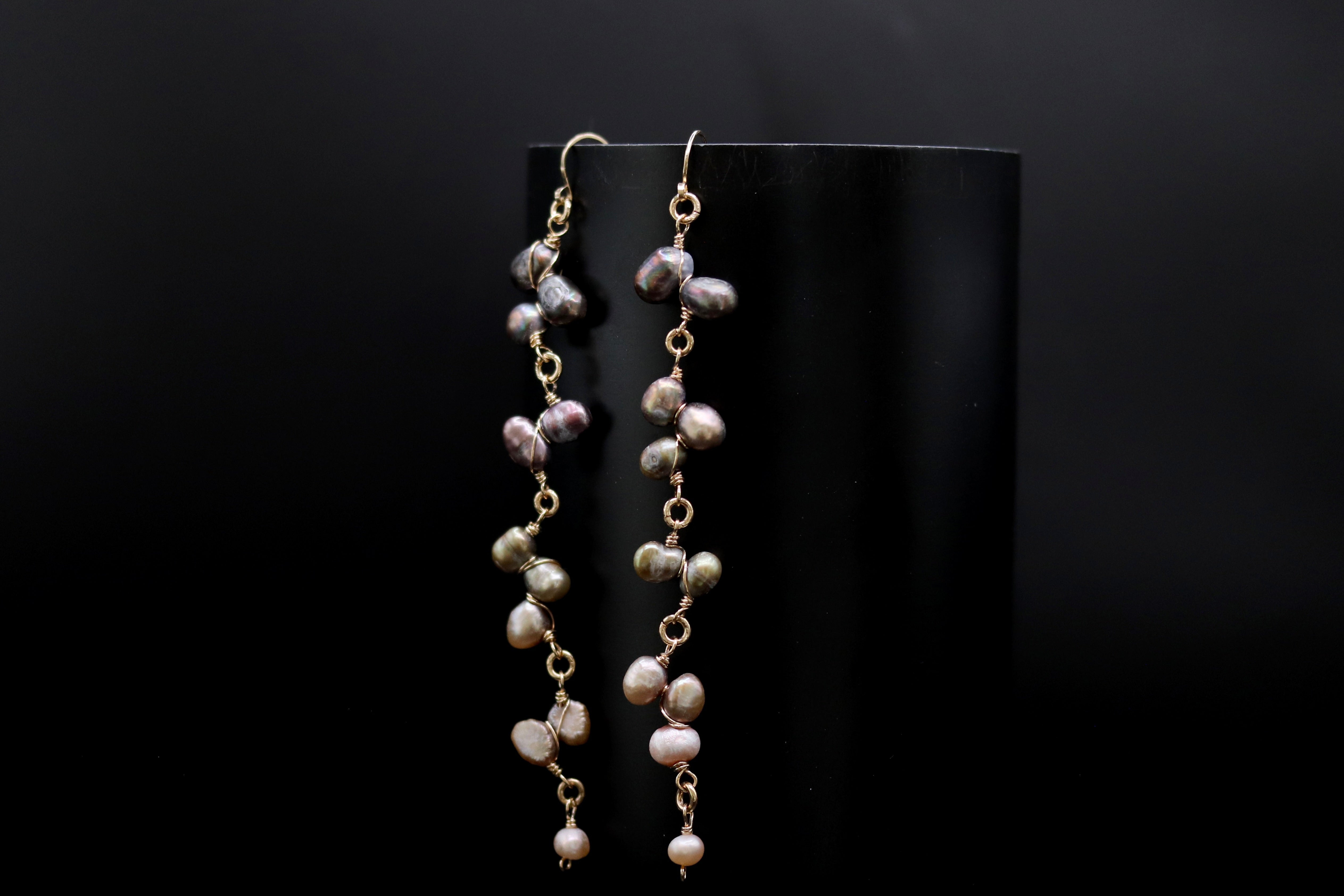 A pair of earrings with multiple strands of pearls hanging from a black background.
