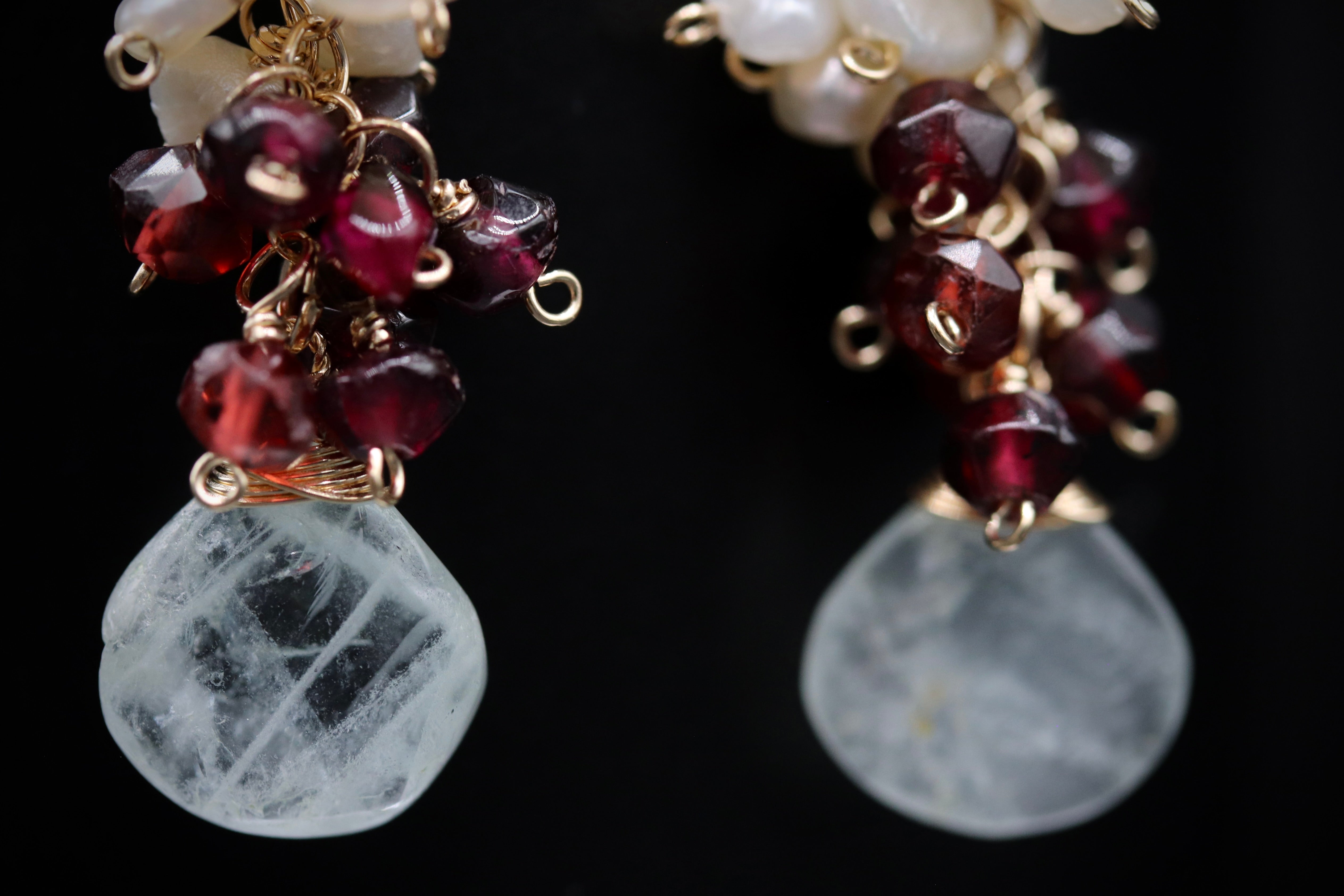 A close-up view of a pair of earrings with a combination of white and maroon gemstones, as well as some metallic beads.