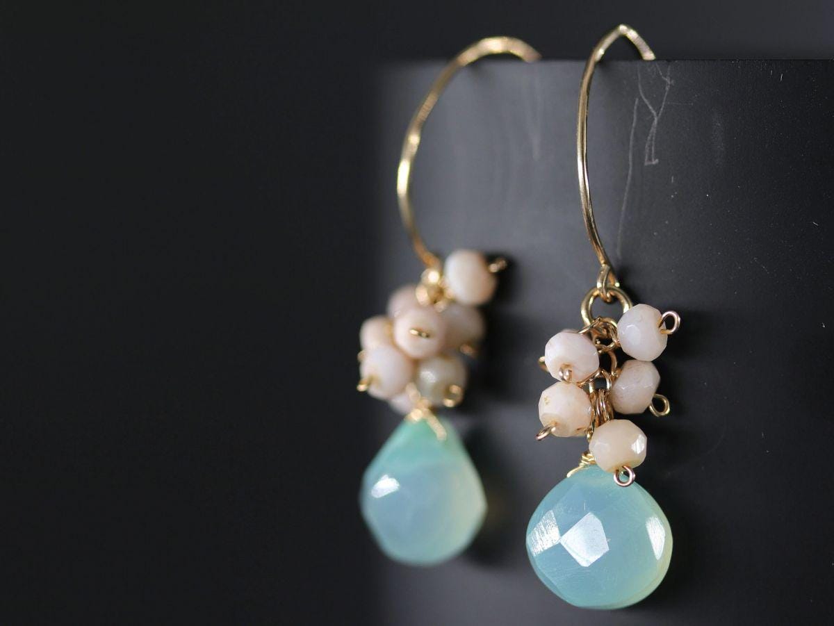 May include: A pair of gold hoop earrings with a cluster of small, light pink beads and a teardrop-shaped, light blue gemstone dangling from each hoop.