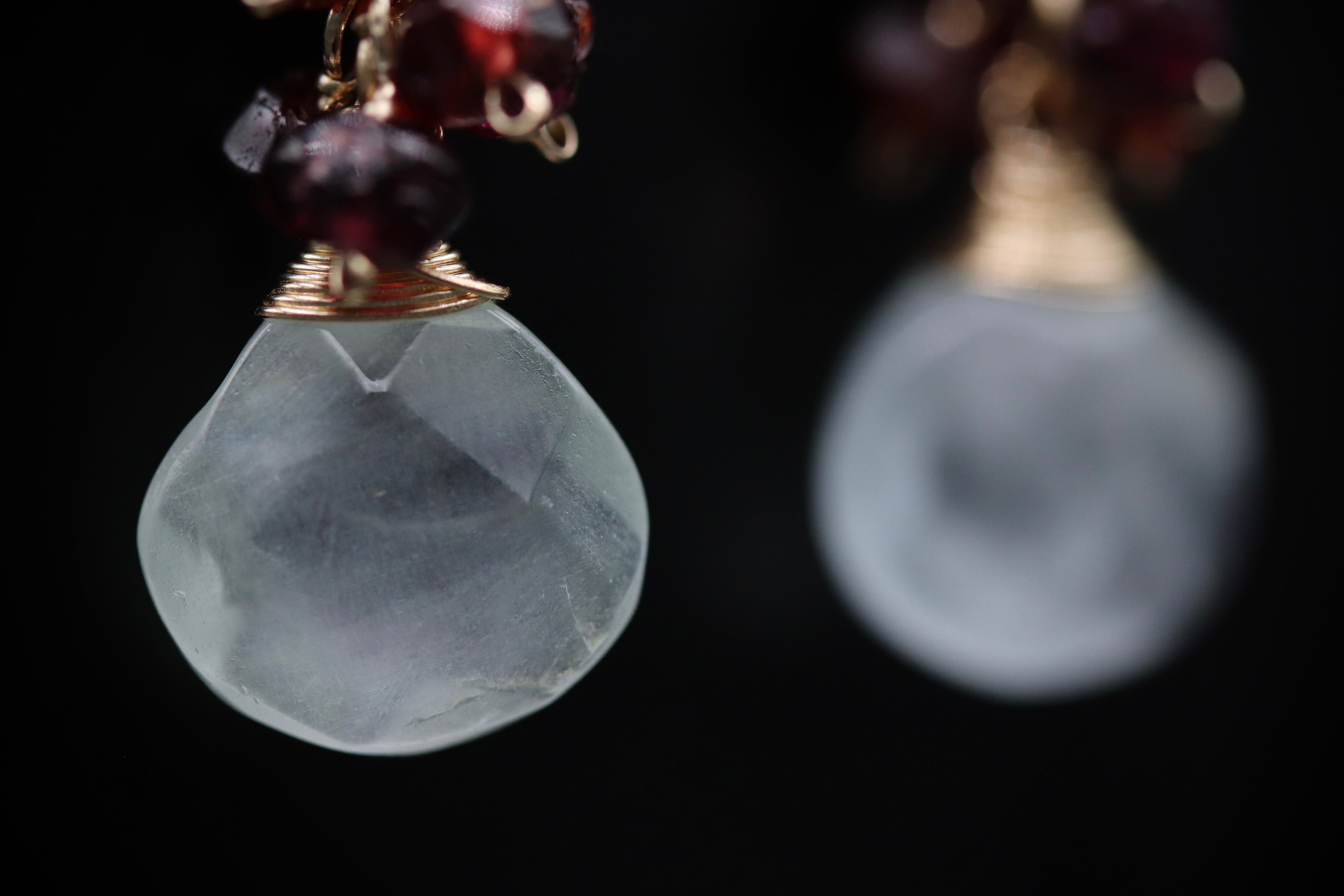 a close-up view of two crystal pendants with a mix of clear and maroon gemstones. The pendants are suspended from a chain, creating a visually appealing and elegant design.