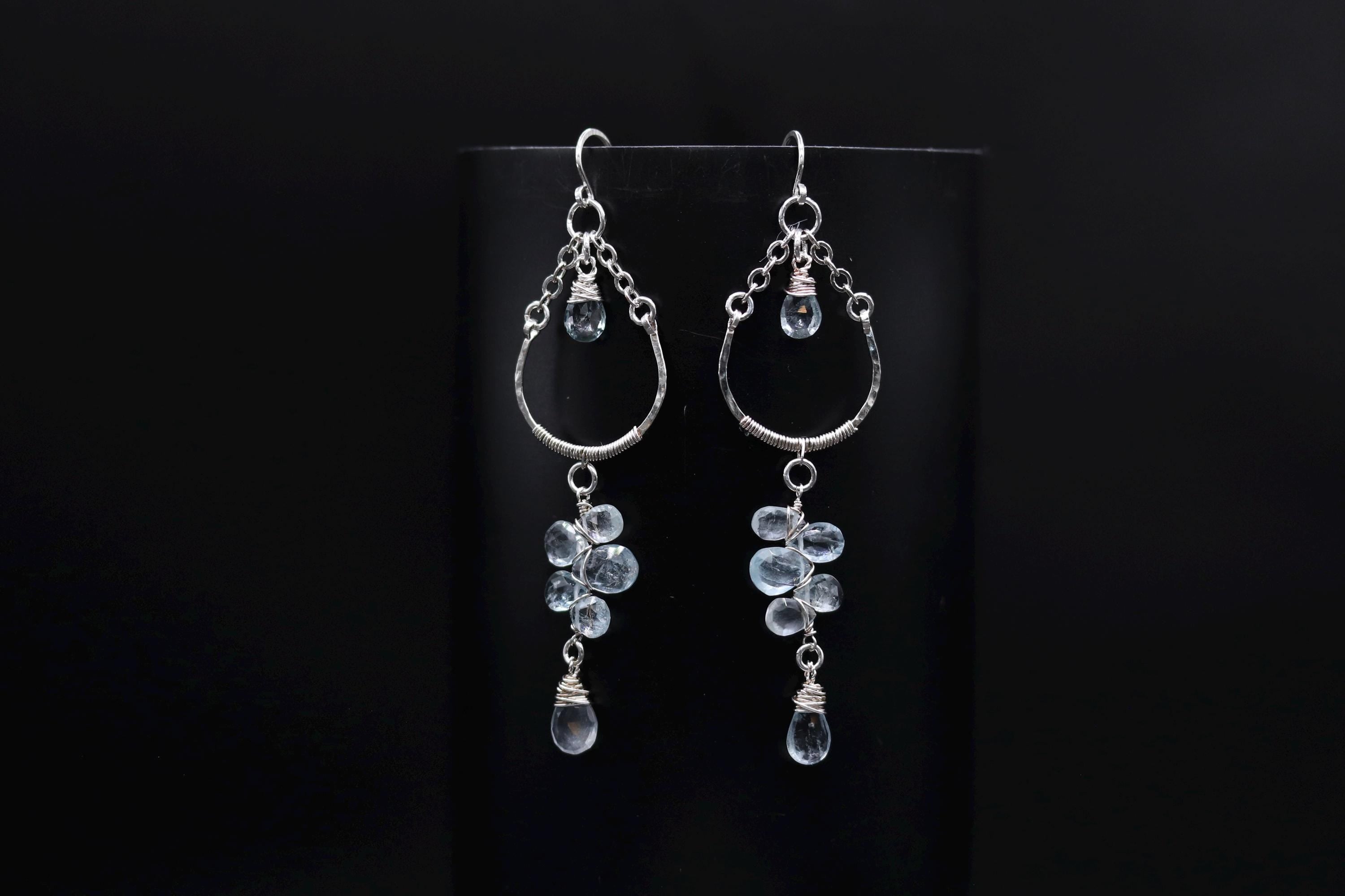 A pair of silver earrings with clear gemstone accents, hanging from the ear hooks against a black background.