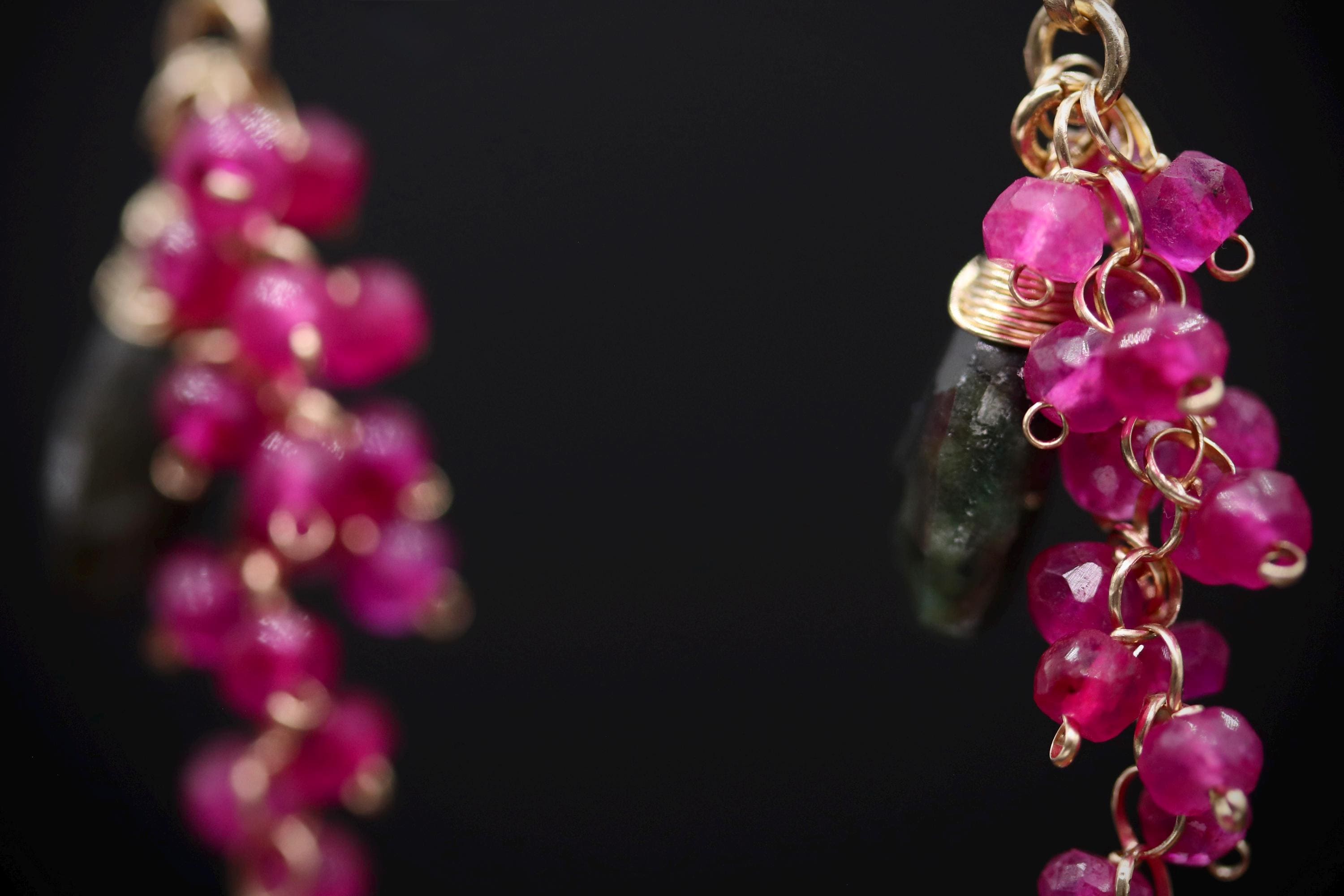 A close-up view of a pair of earrings with a combination of pink gemstones and metallic chains.