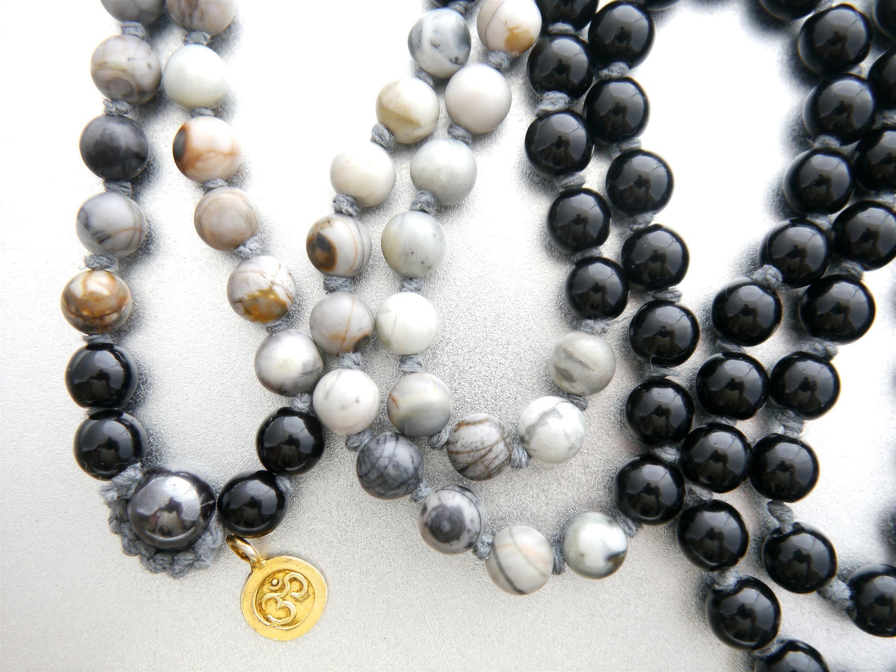 a collection of beaded necklaces, with a gold pendant featuring the Om symbol. The necklaces are made of various materials, including black and gray beads, and the arrangement of the beads creates a visually appealing display.