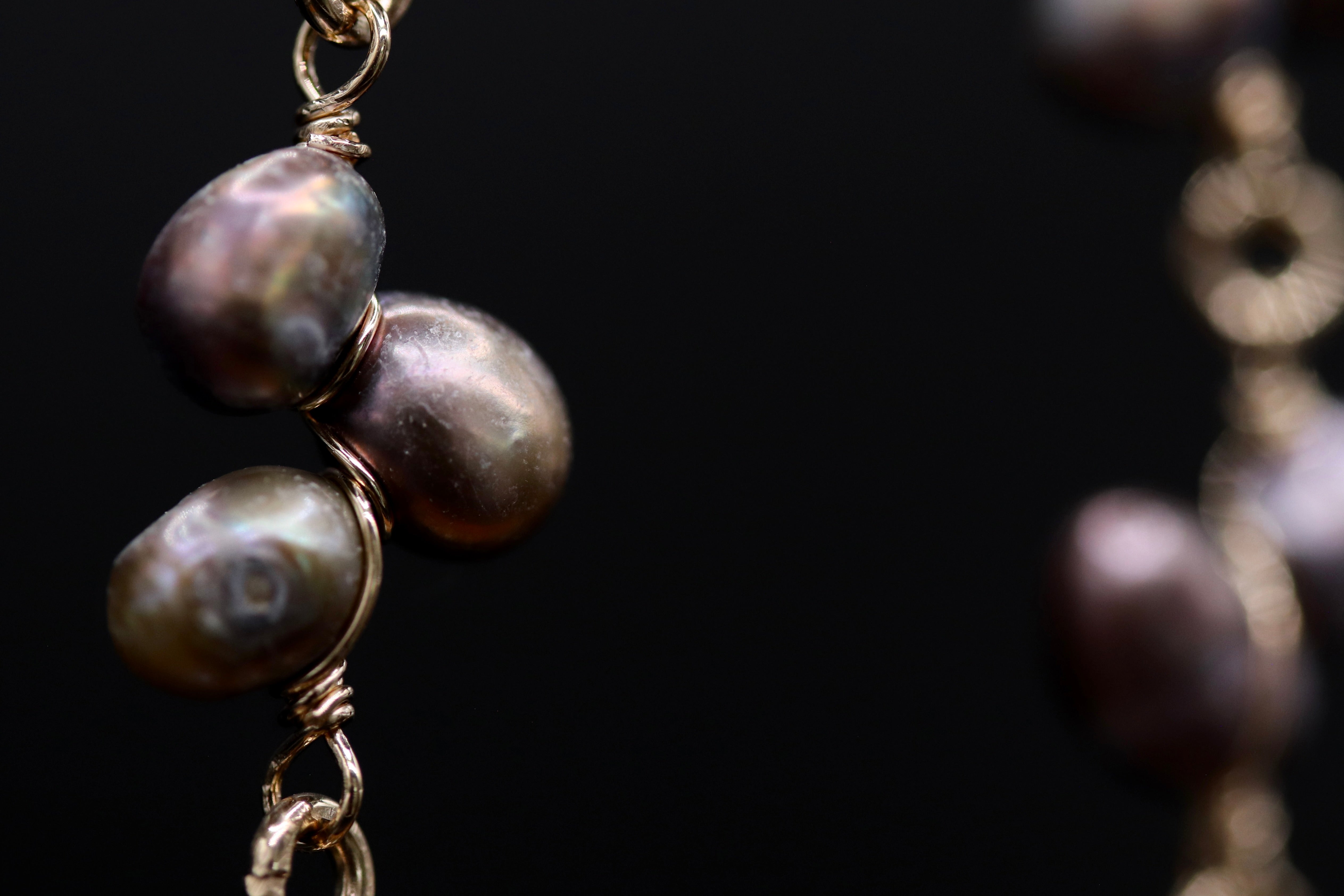 A close-up view of a chain with two large, round pearls attached to it, set against a dark background.