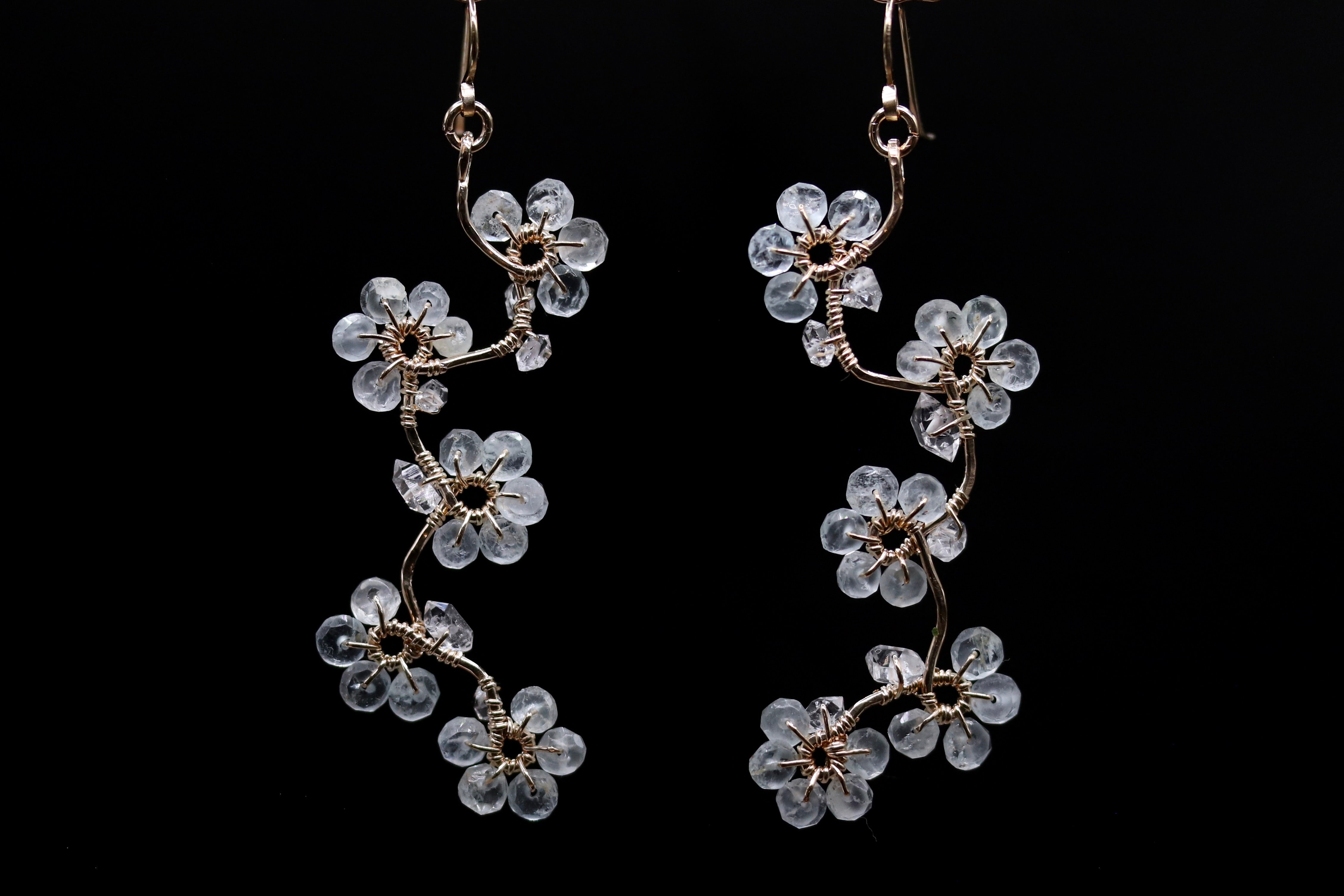 A pair of delicate earrings with clear crystal flowers on a black background.