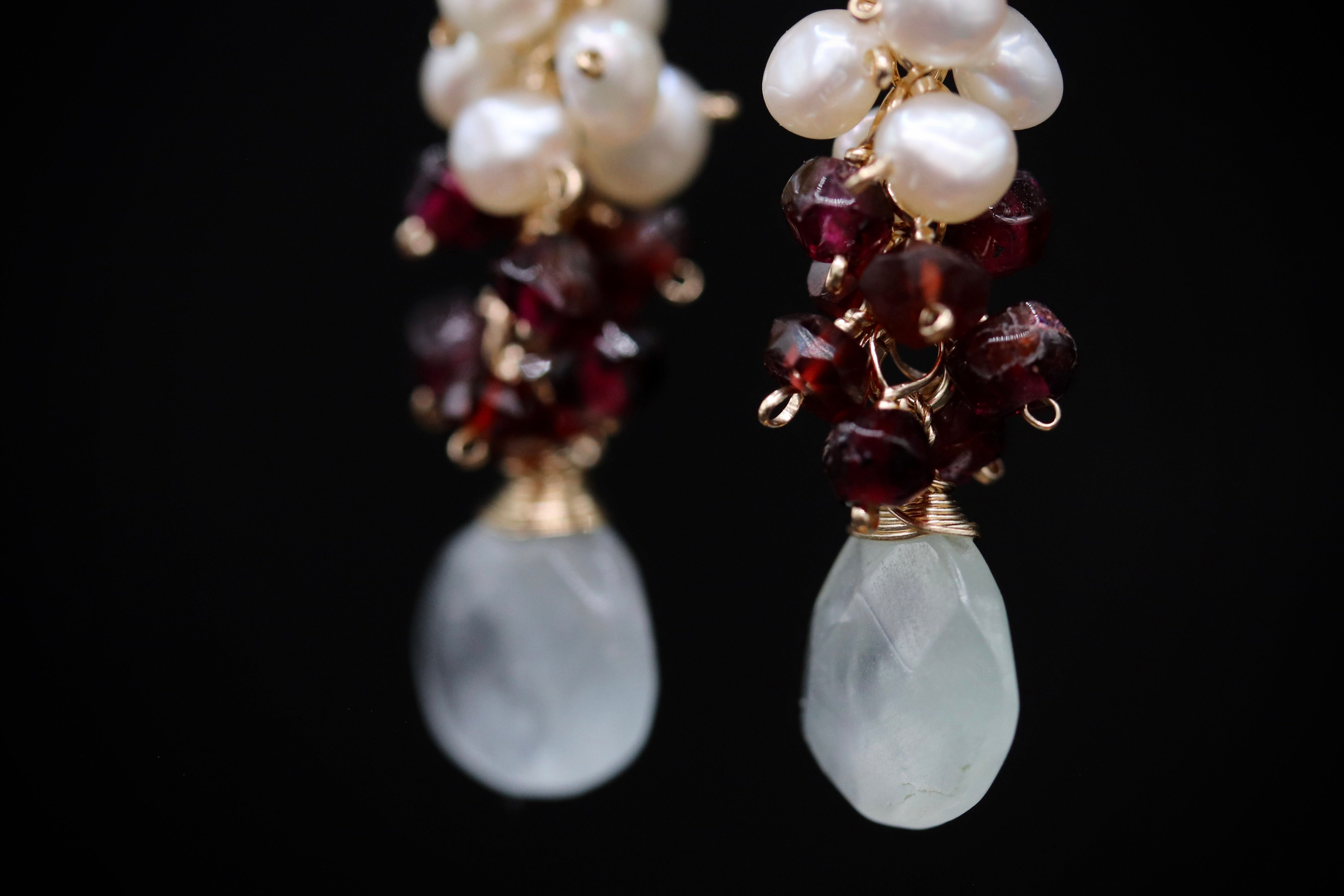 A close-up view of a pair of earrings with white and maroon gemstones and gold-colored metal accents.
