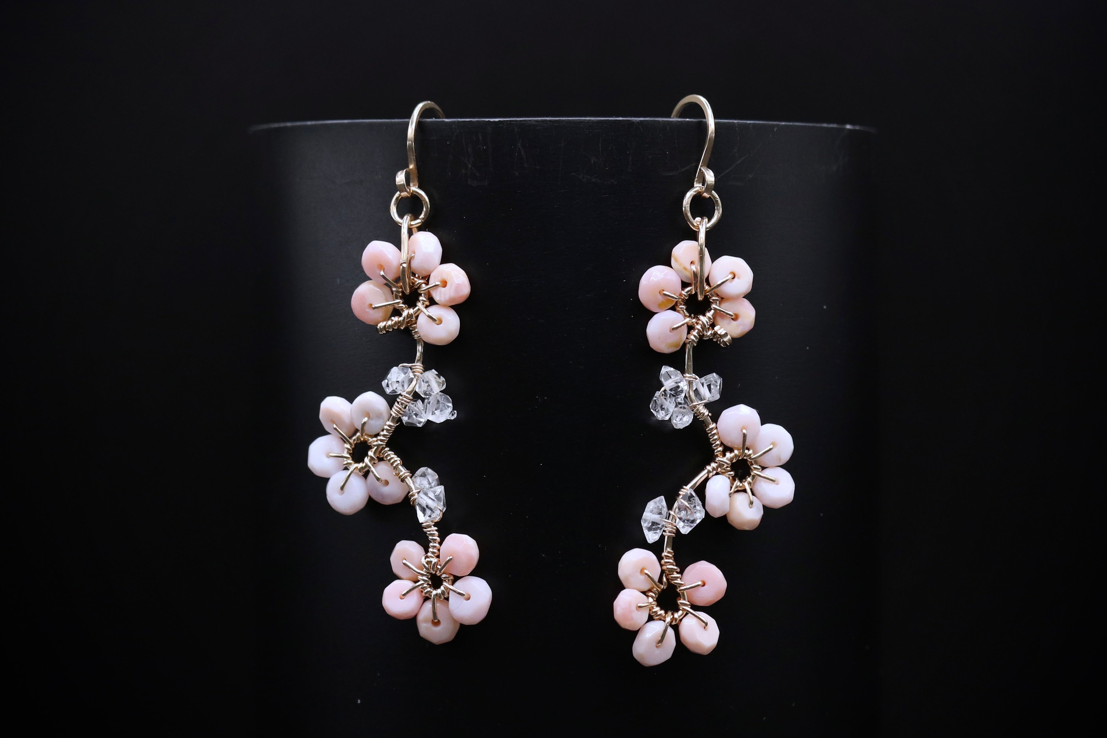 A pair of delicate earrings with small white flowers and clear gemstones hanging from the bottom of the earrings against a black background.