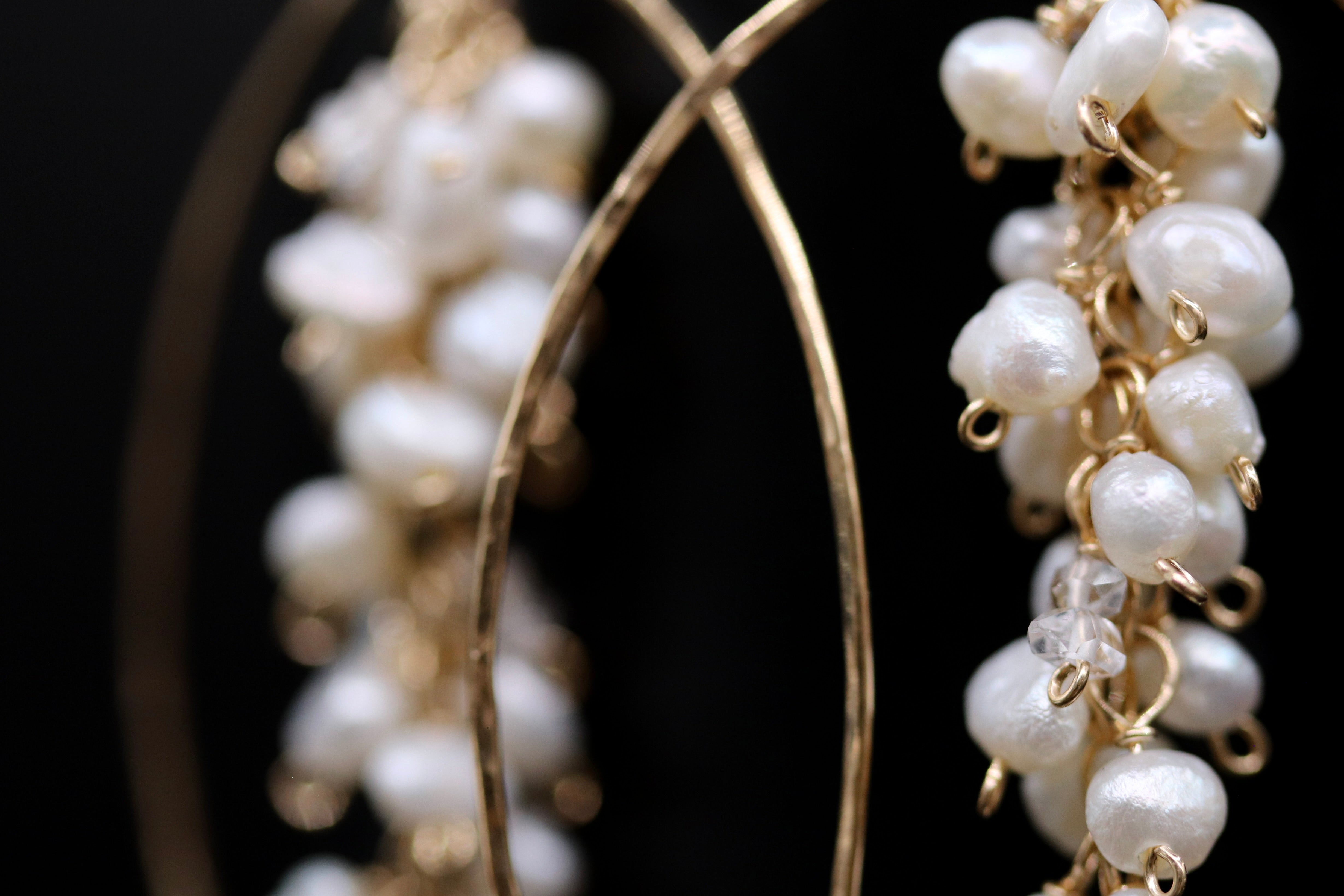 A close-up view of a pair of delicate earrings, with a focus on the intricate design and the dangling white pearls.