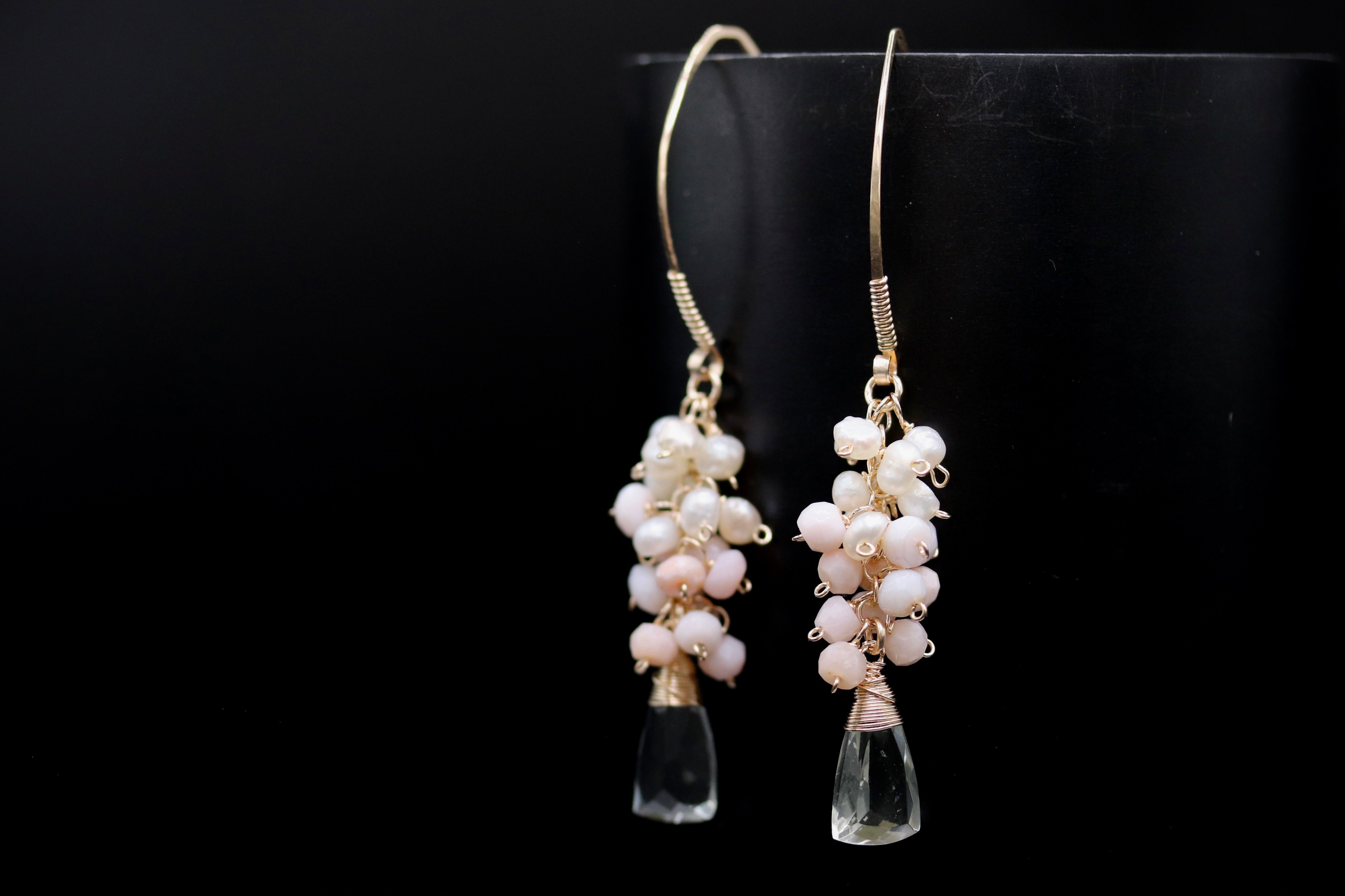 A pair of elegant earrings with clear gemstone pendants and white pearl accents, displayed against a black background.
