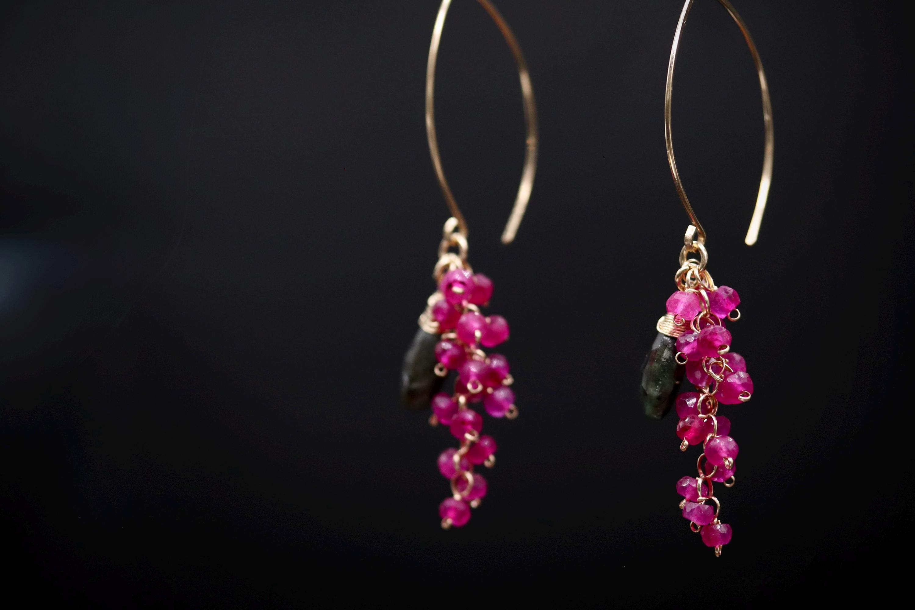 A pair of earrings with a dark background, featuring a gold hoop and dangling earrings with pink gemstones.