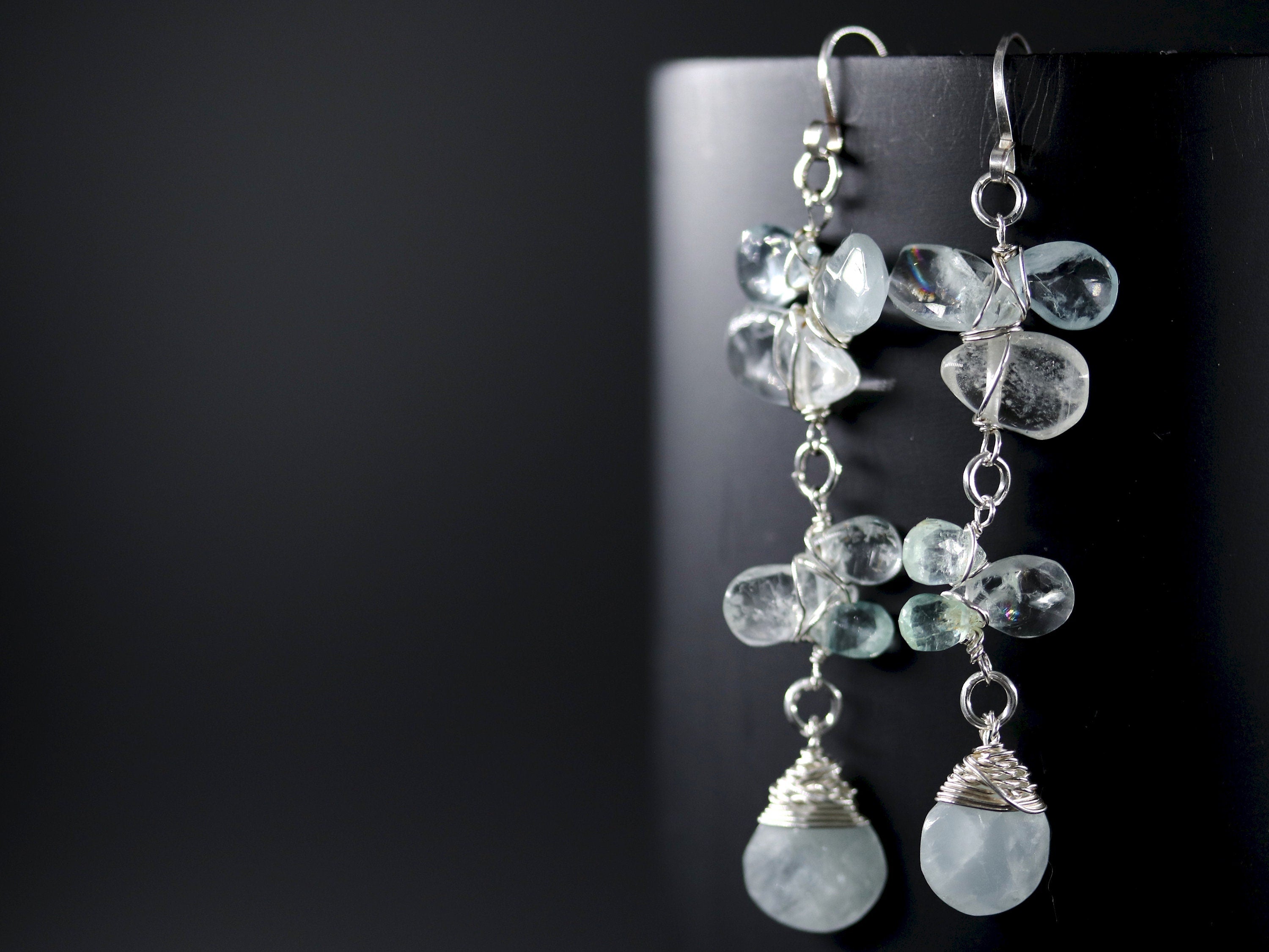 May include: Silver dangle earrings with multiple light blue aquamarine stones wrapped in silver wire.