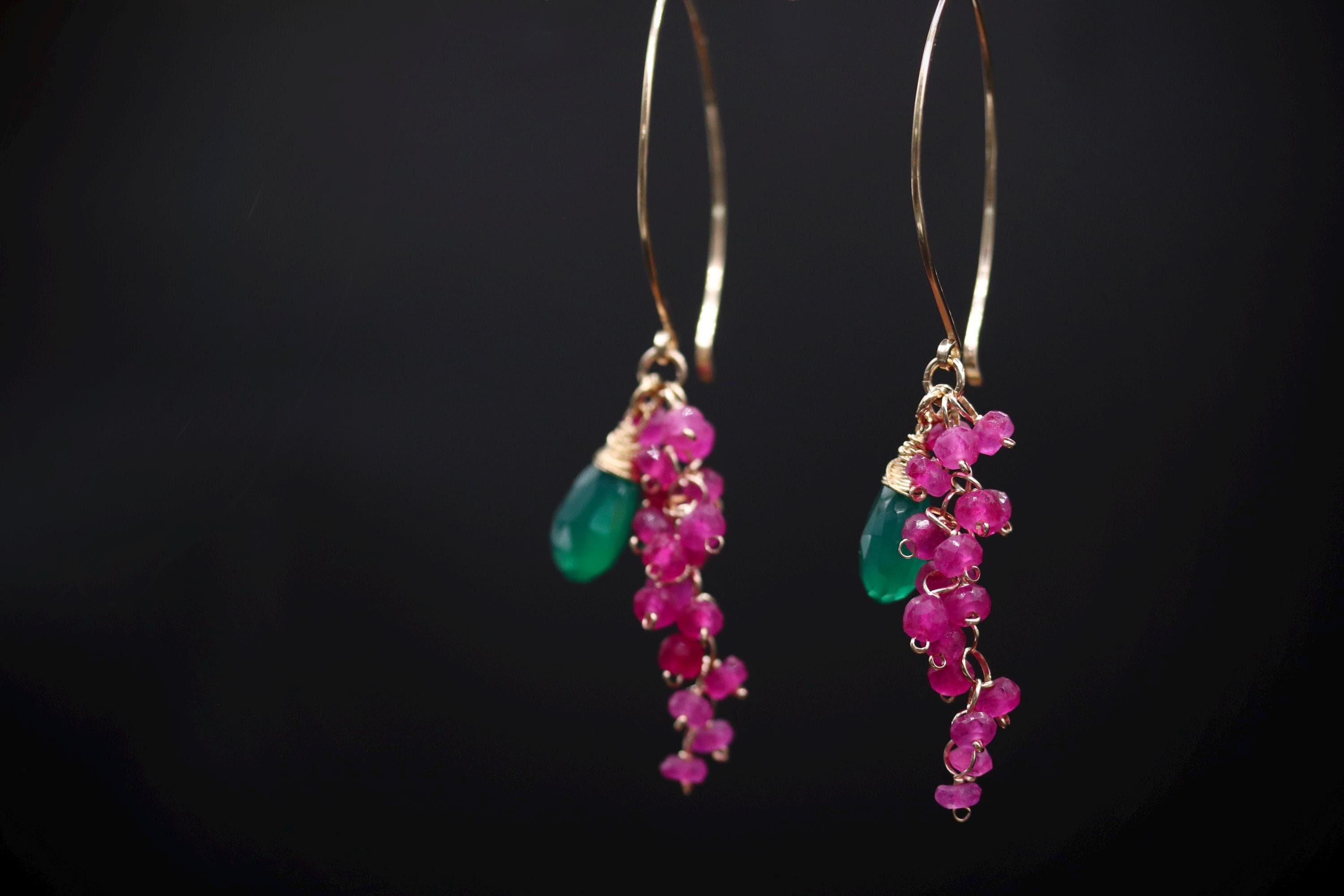 A pair of earrings with green and pink gemstones hanging from a gold hoop.