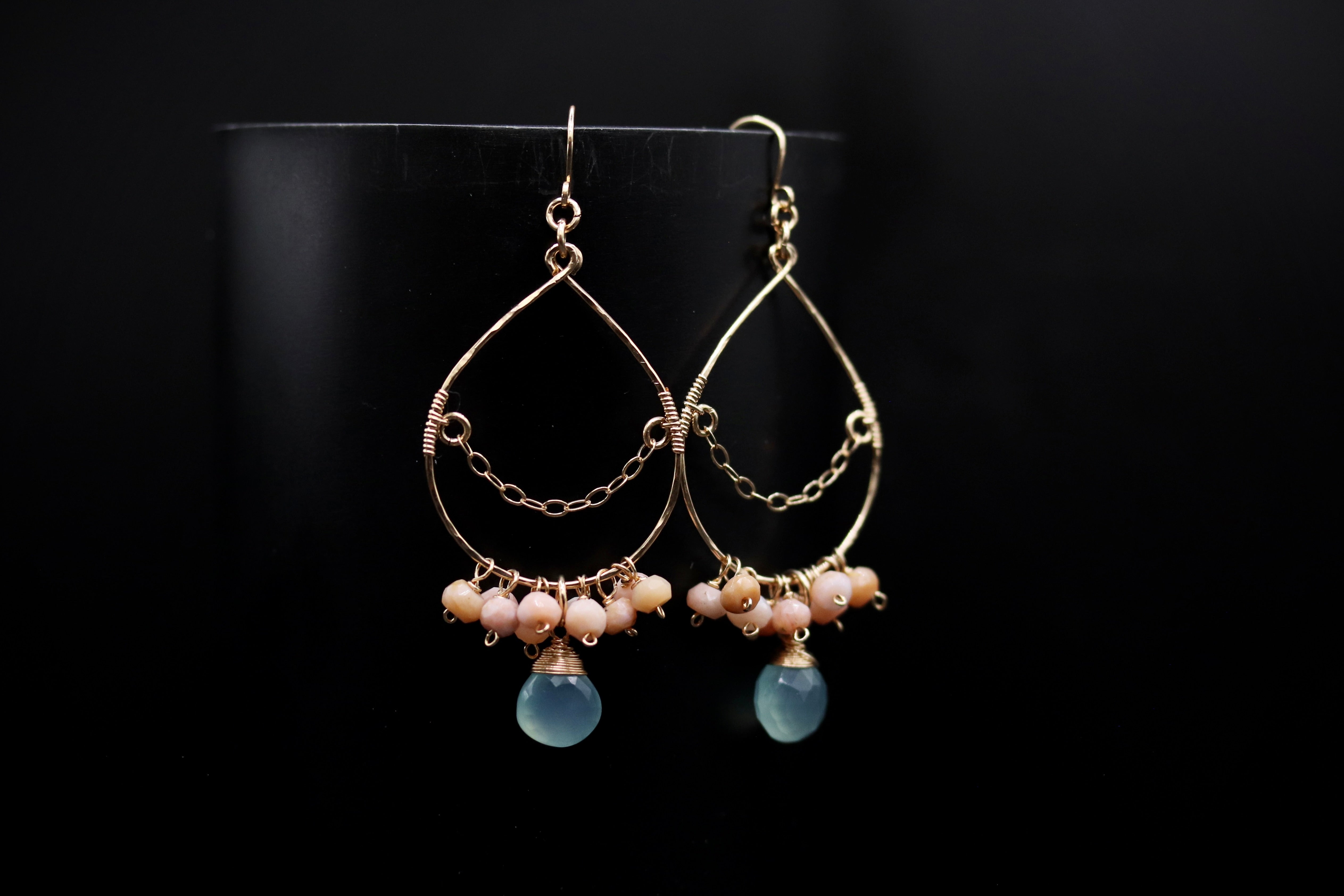 A pair of gold earrings with blue gemstones and dangling chains against a black background.