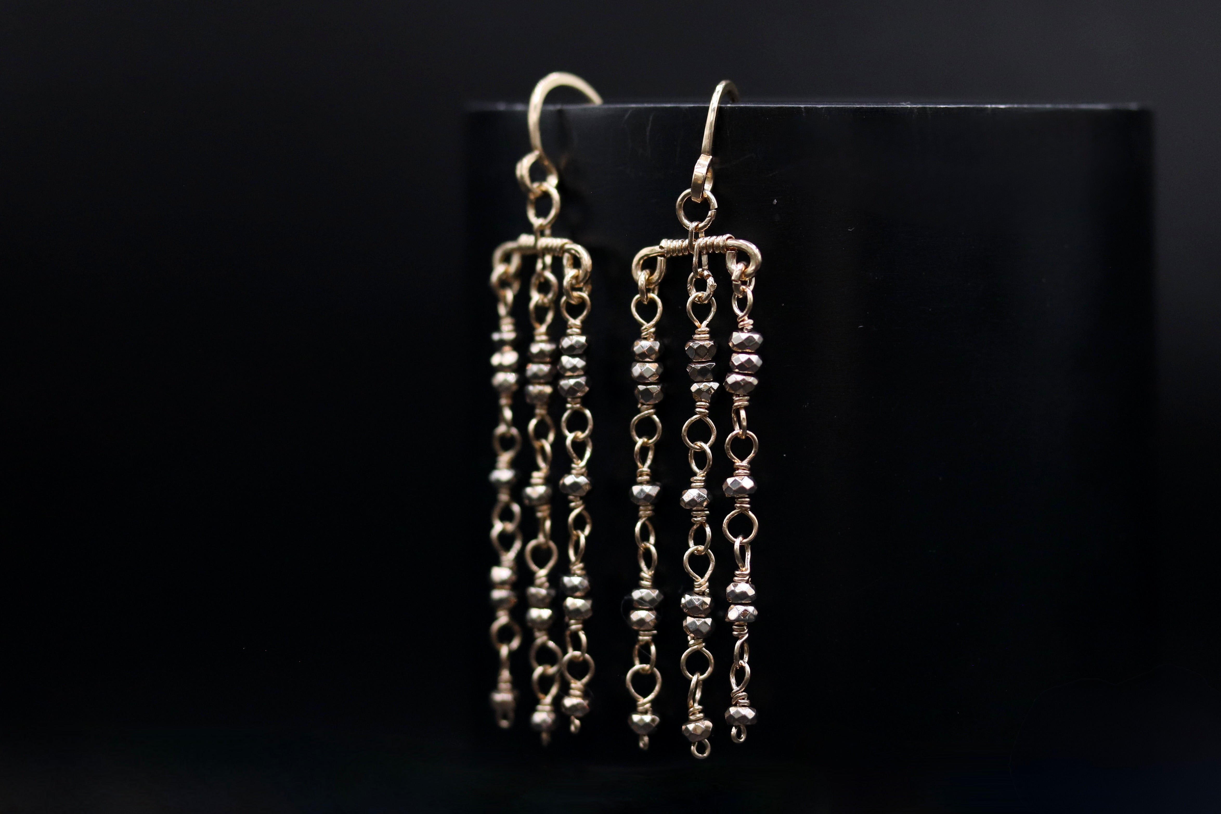 A pair of elegant silver earrings with dangling metal beads, displayed against a dark background.