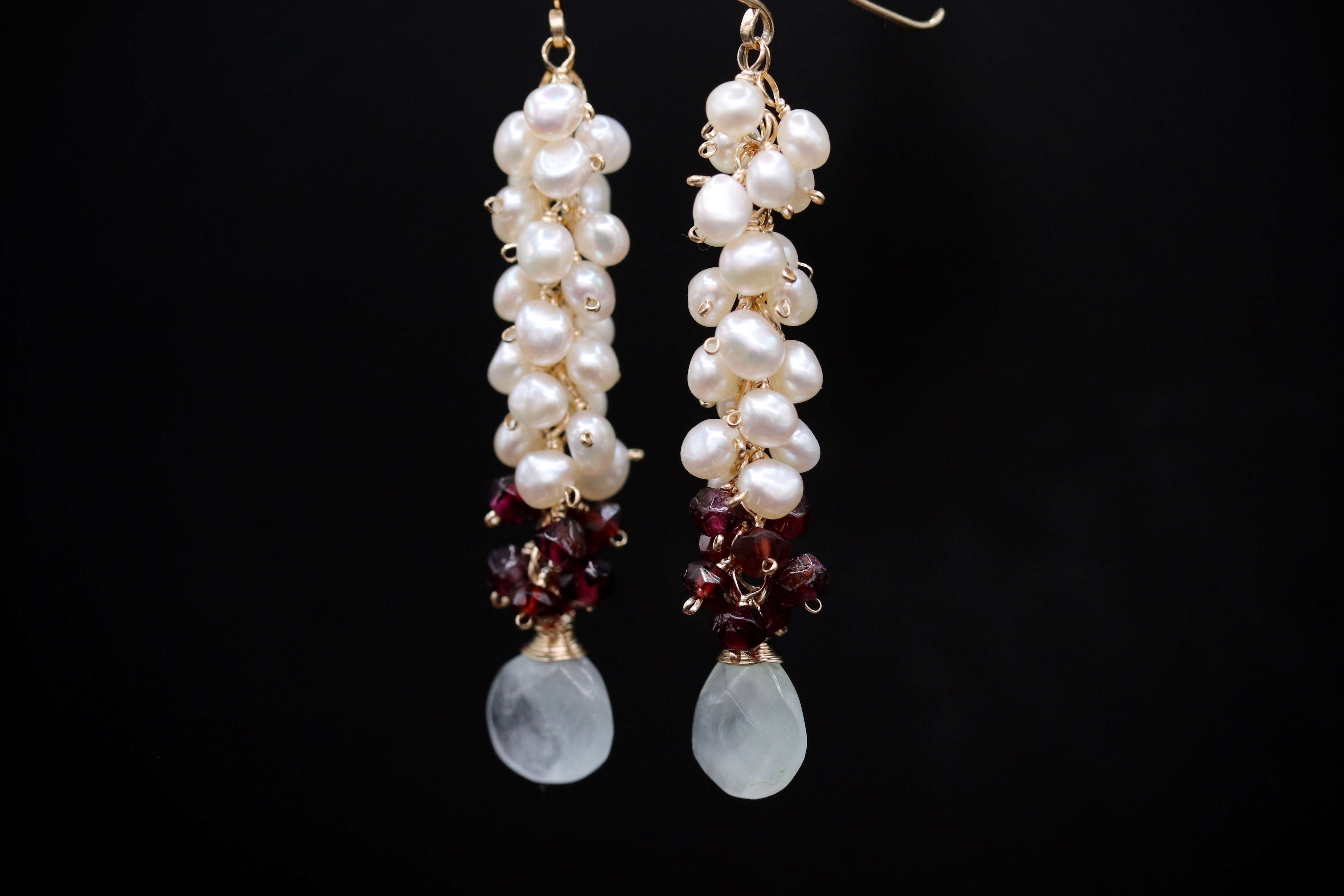 A pair of elegant earrings with white pearls and burgundy gemstones hanging from the ends.