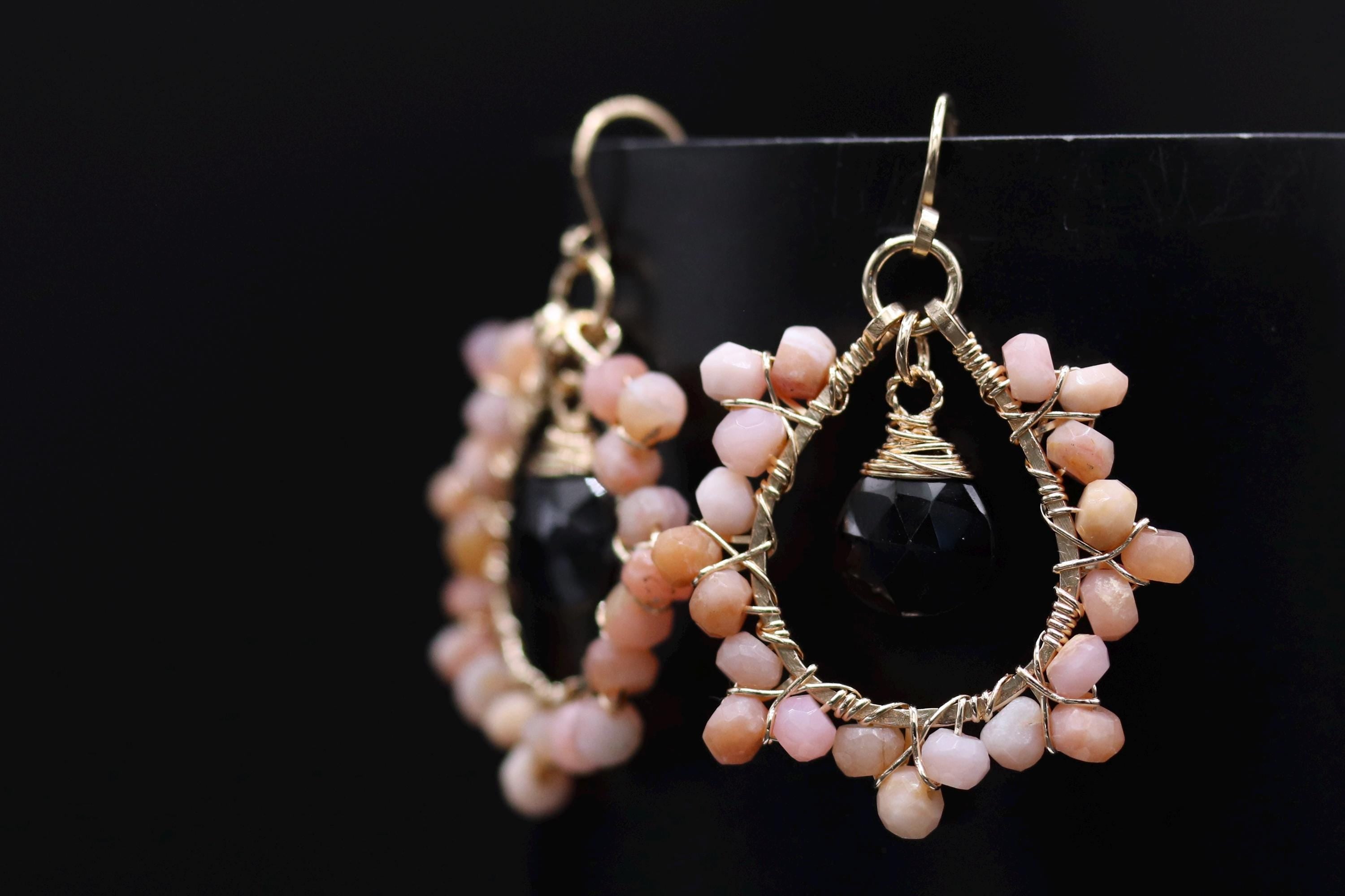A pair of elegant earrings with a black stone and a cluster of pink and white beads, set against a black background.