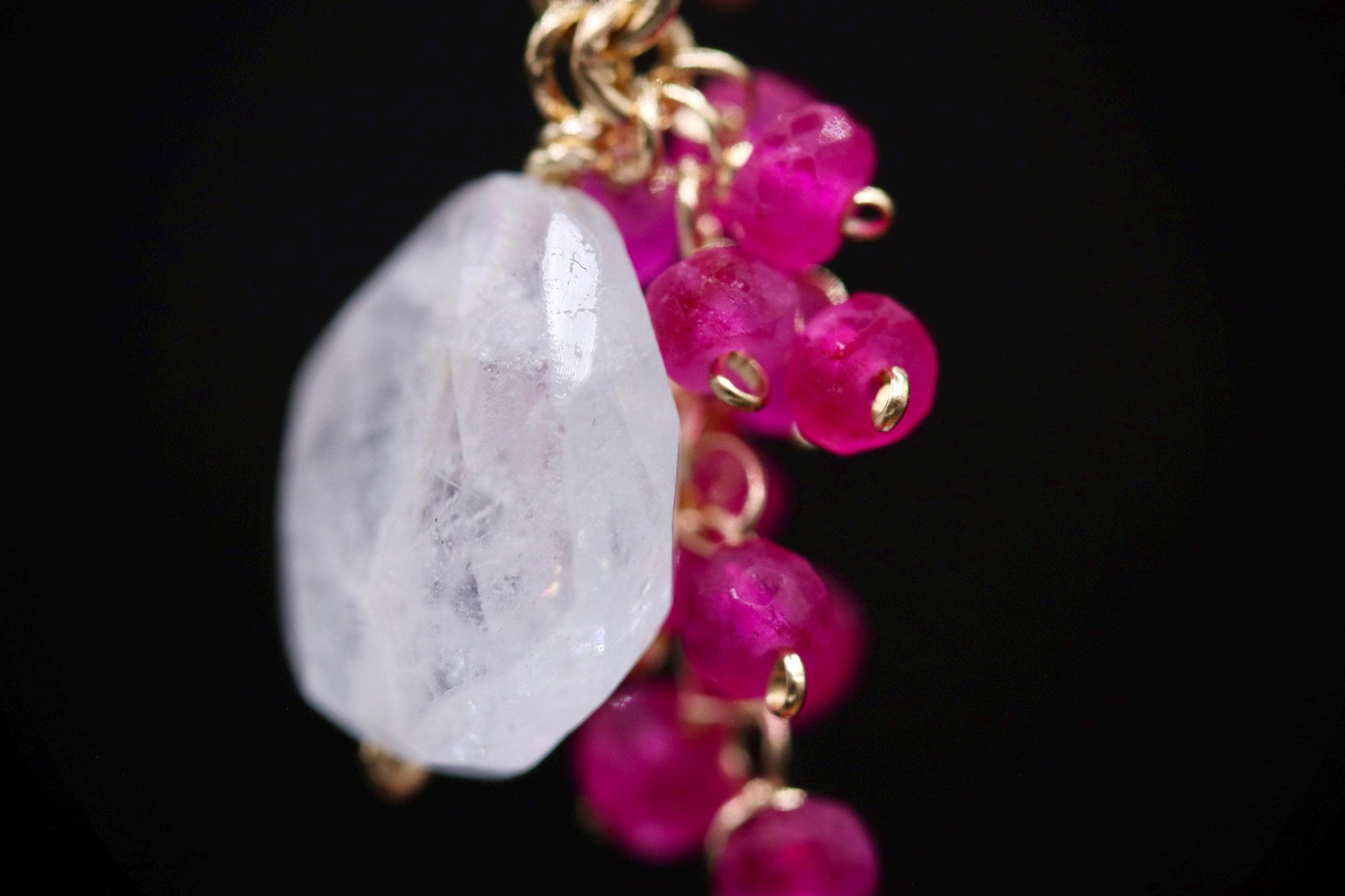 A close-up image of a piece of jewelry with a clear gemstone and a cluster of small, round, pink gemstones.