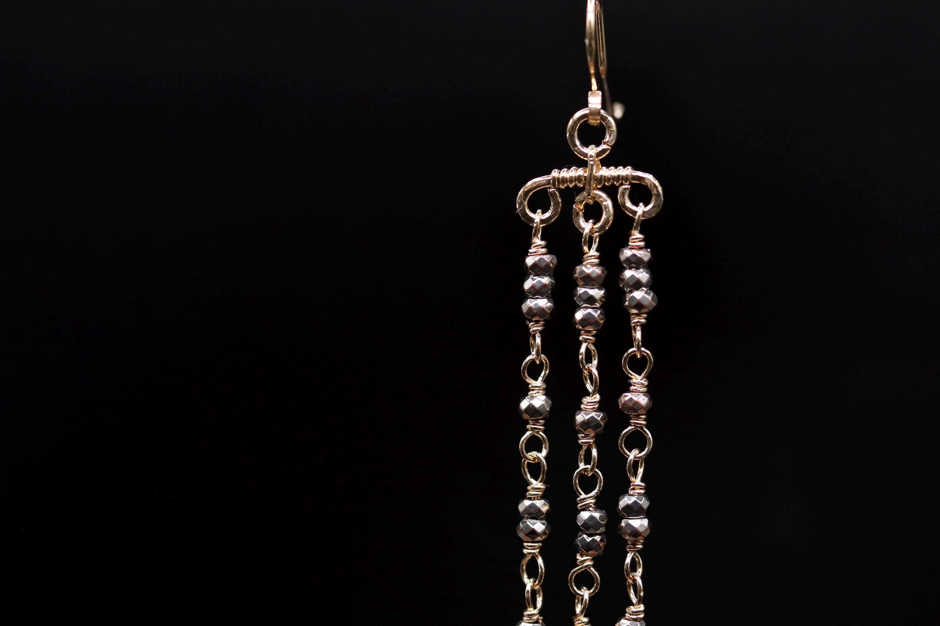 A close-up view of a decorative earring with multiple tiers of small, round beads or stones attached to a hook or chain.