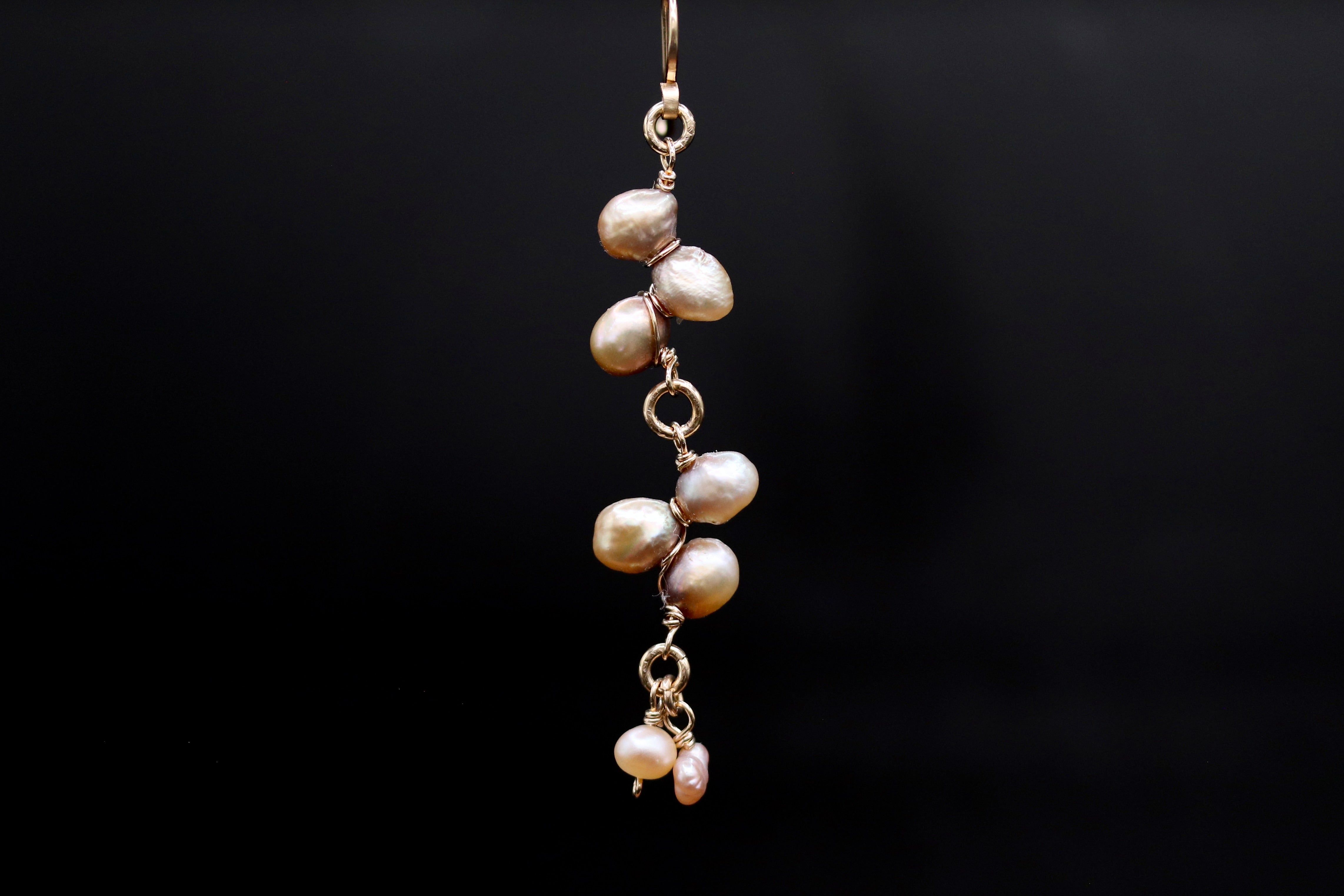 A close-up view of a delicate earring with a cluster of small, round pearls suspended from a gold-colored metal hook against a dark background.