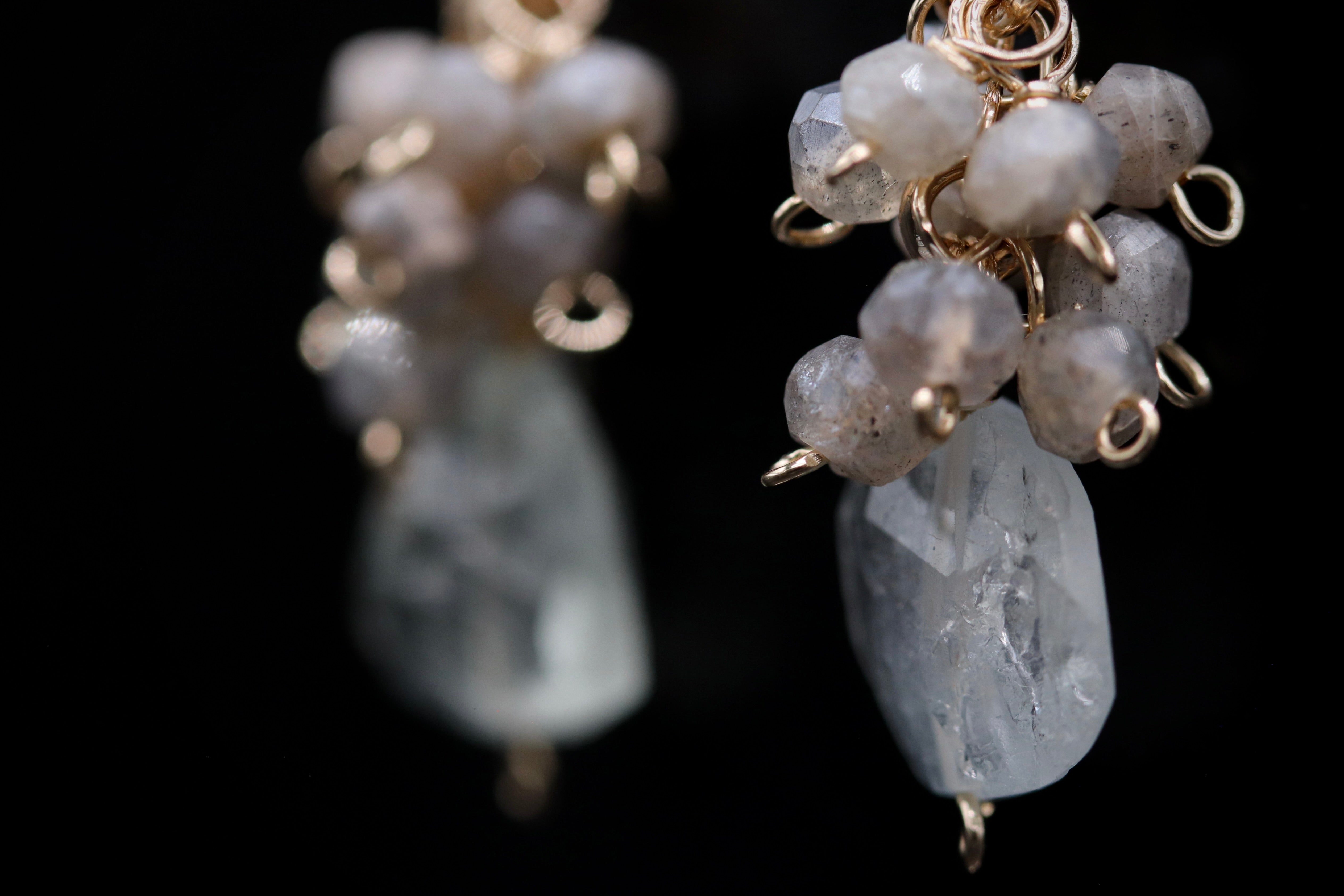 A close-up view of a pair of earrings with a combination of clear gemstones and metallic wire elements.