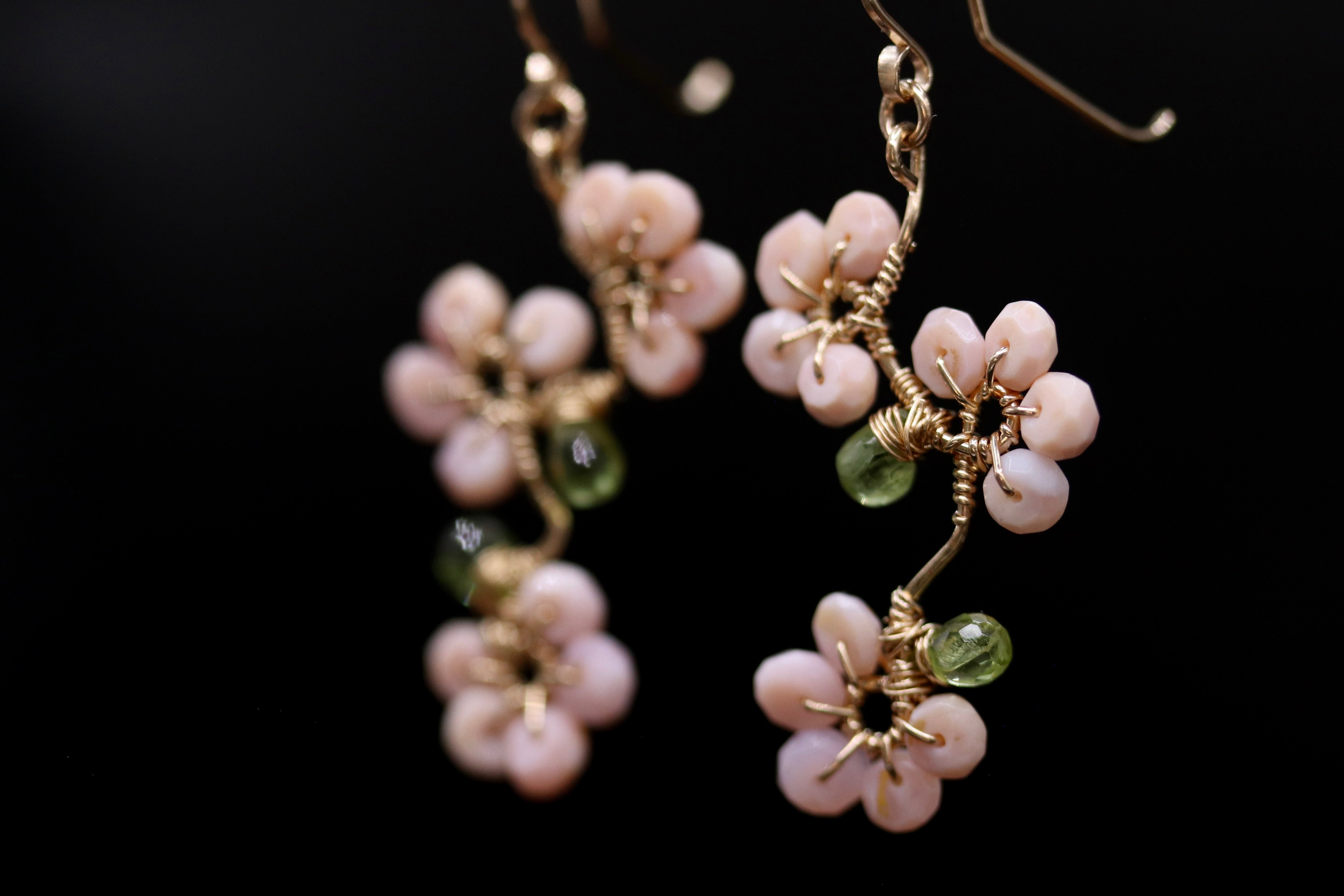 A pair of delicate earrings with pink and green beads, each adorned with a small green bead at the center.