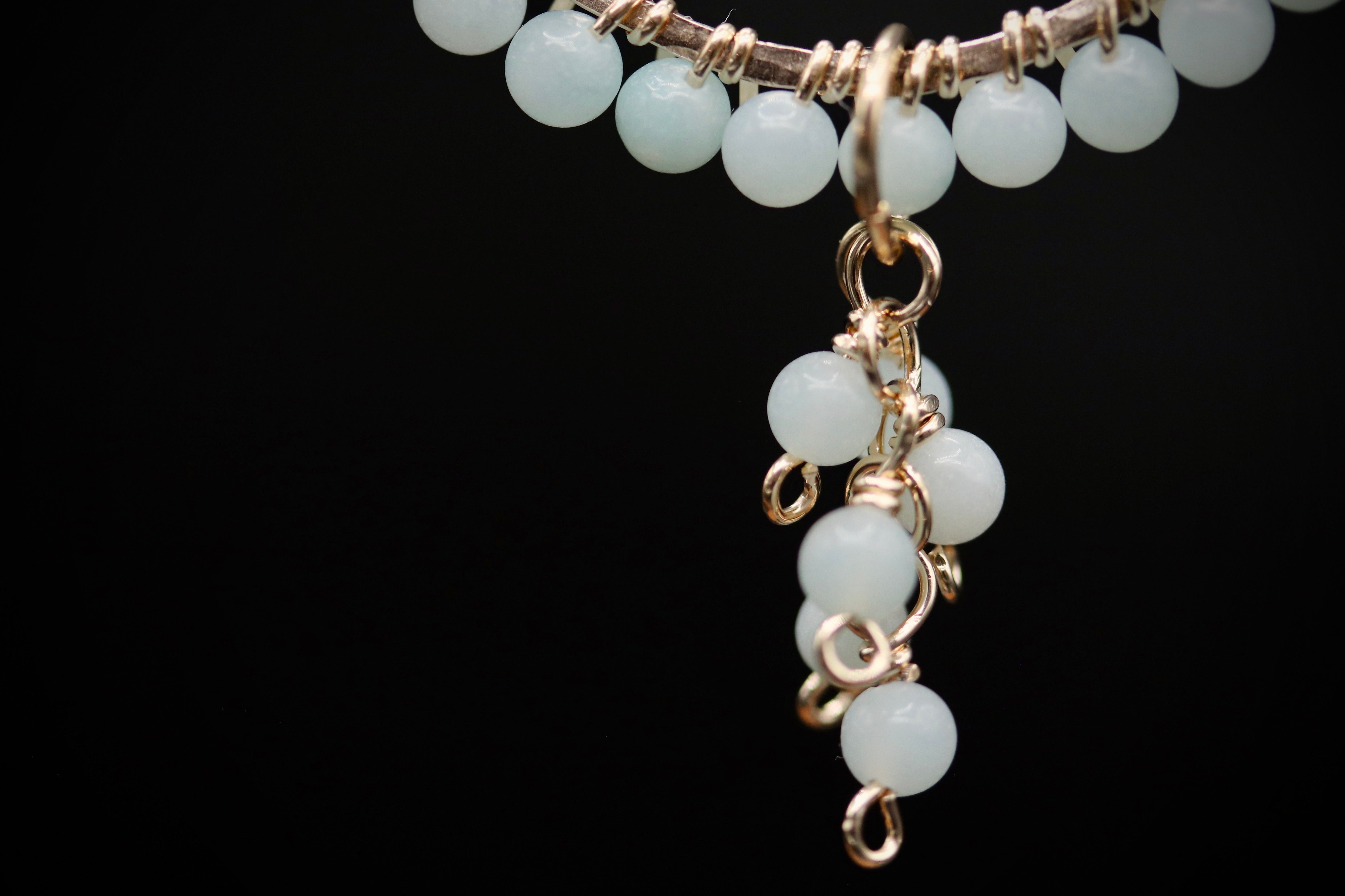 A close-up view of a delicate necklace with a pendant made of small white beads, suspended from a chain against a black background.